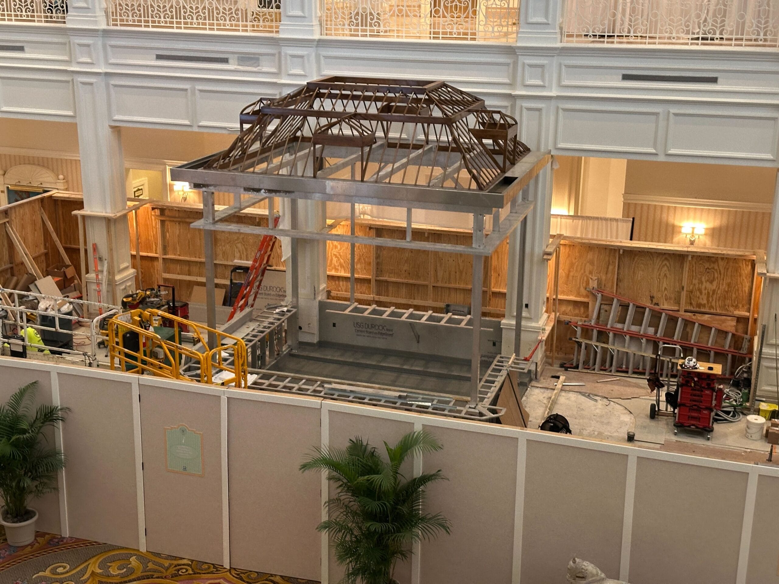 Construction workers build a gazebo-like Tea Room inside a grand indoor space with white walls and railings.
