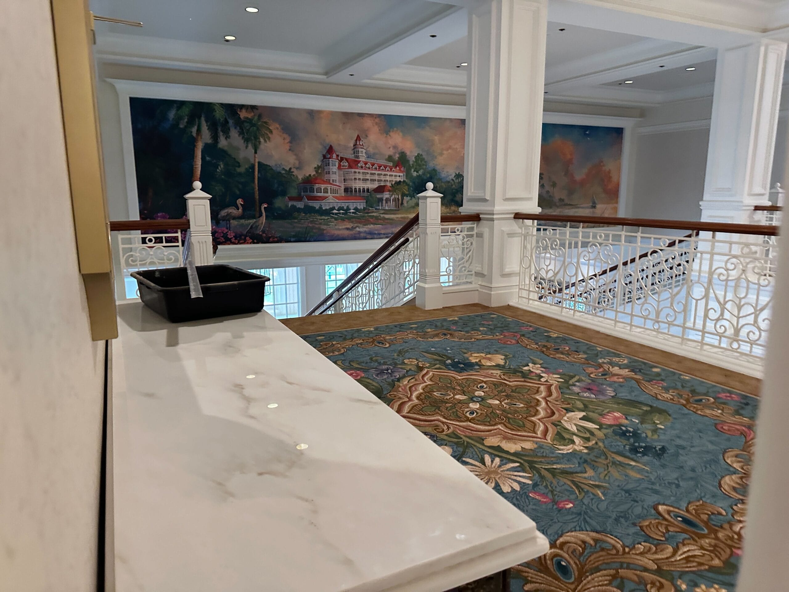 A marble countertop overlooks a stairway with ornate railings and a mural of a grand building in the background.