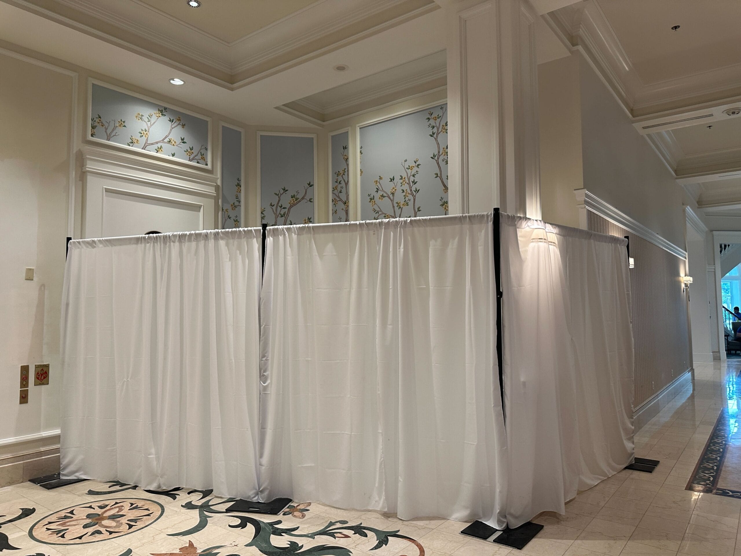White curtains enclose a corner area in a hotel hallway with floral wall accents and patterned tile flooring.