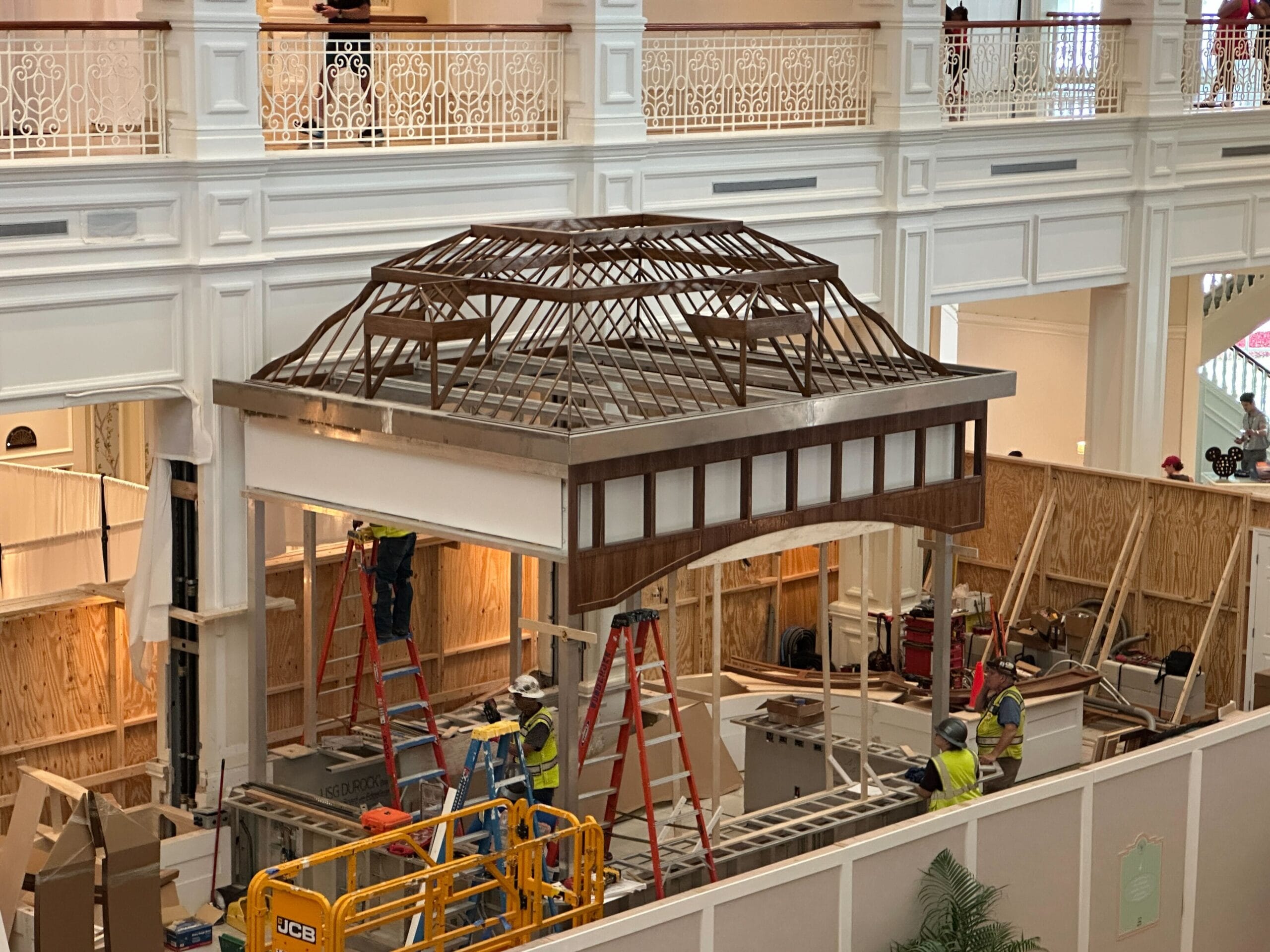 Workers assemble a large wooden gazebo in the lobby, surrounded by scaffolding and new light fixtures at Disney's Grand Floridian Resort.