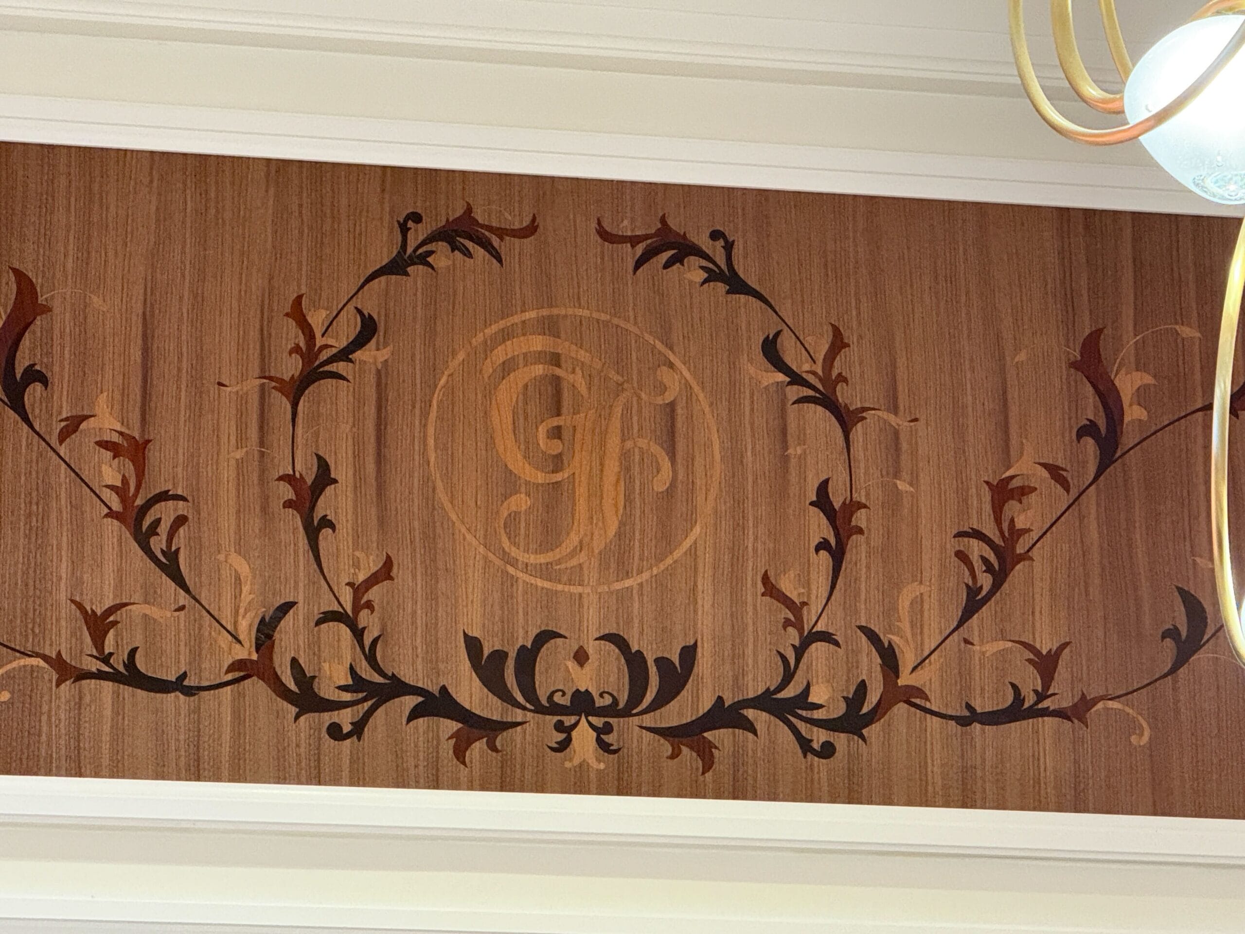 Wood panel with ornate dark and light leaf designs, featuring an elegant GF monogram in the center.