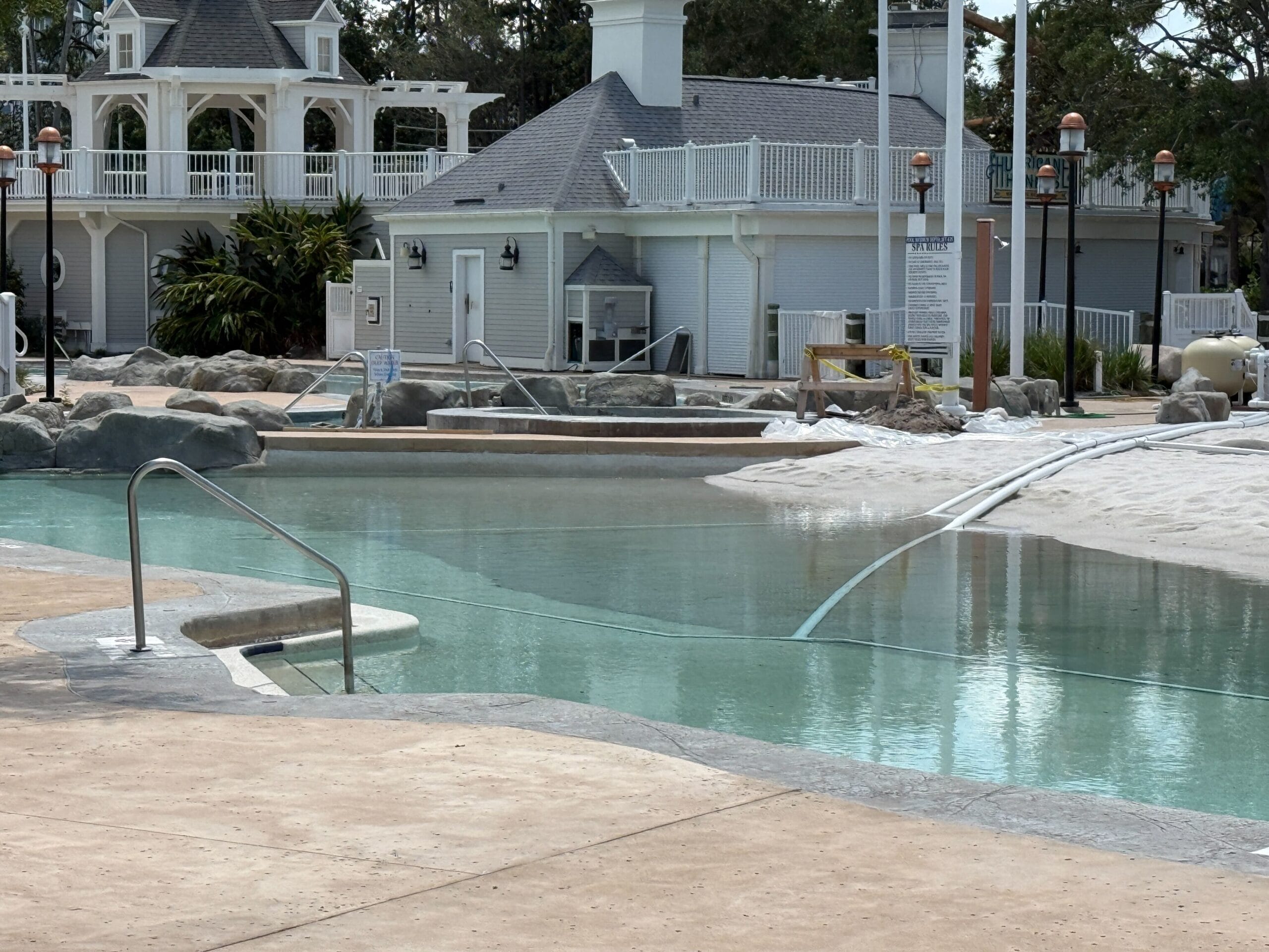 A quiet swimming pool with clear water and steps, surrounded by white buildings and landscaping.