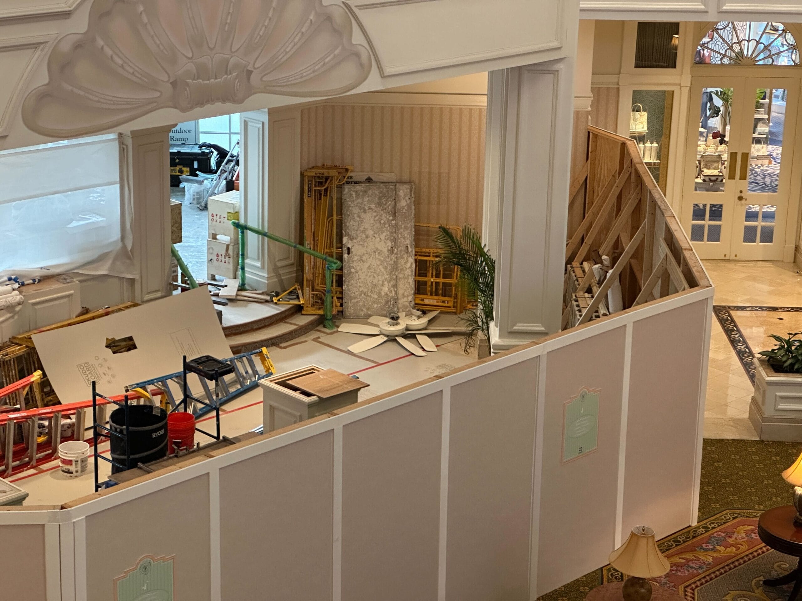 Hotel lobby under renovation with construction materials, ladders, and exposed framing behind temporary white barriers.