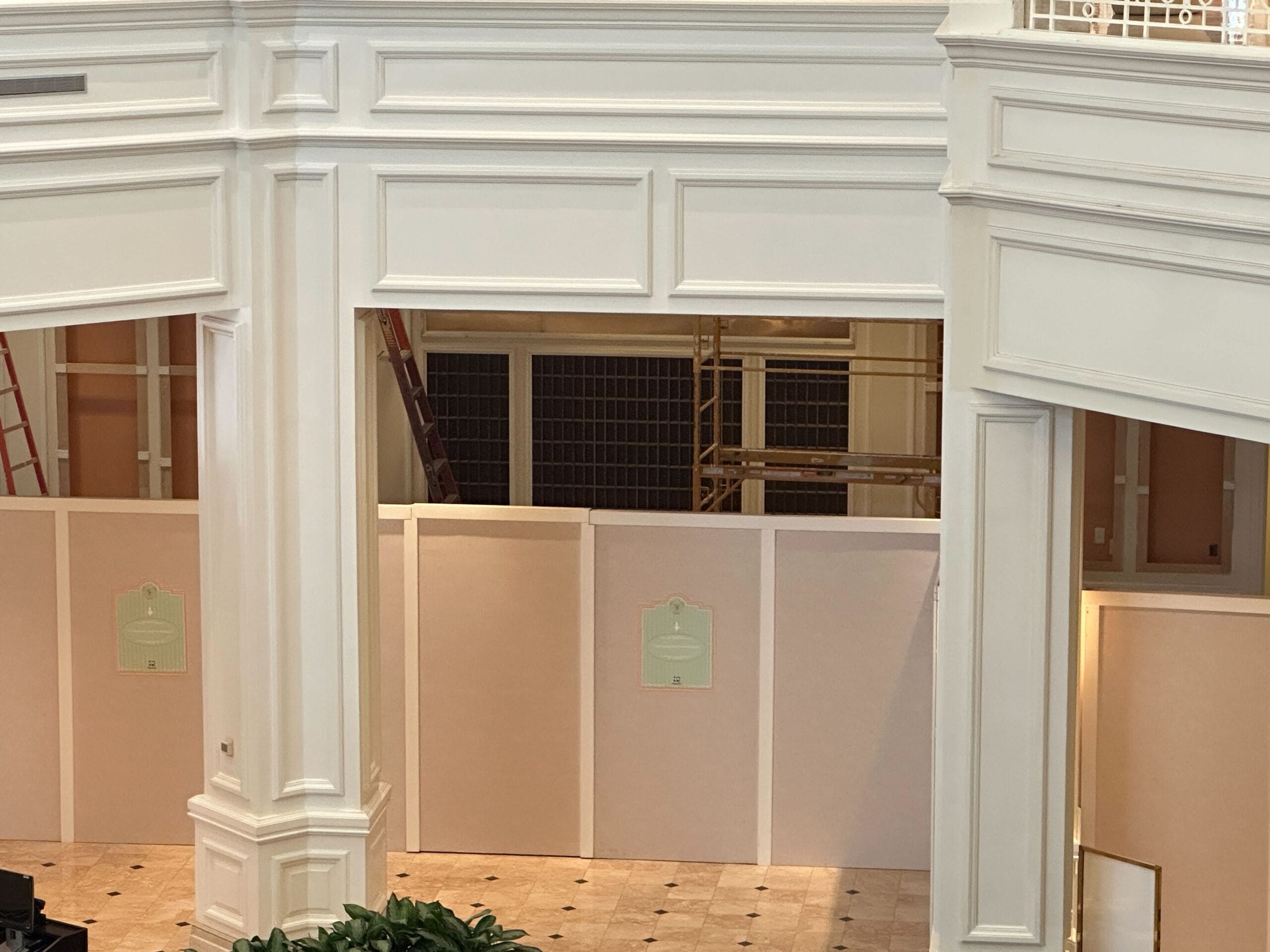 White-paneled construction walls in a building lobby with ladders and scaffolding visible behind the barrier.