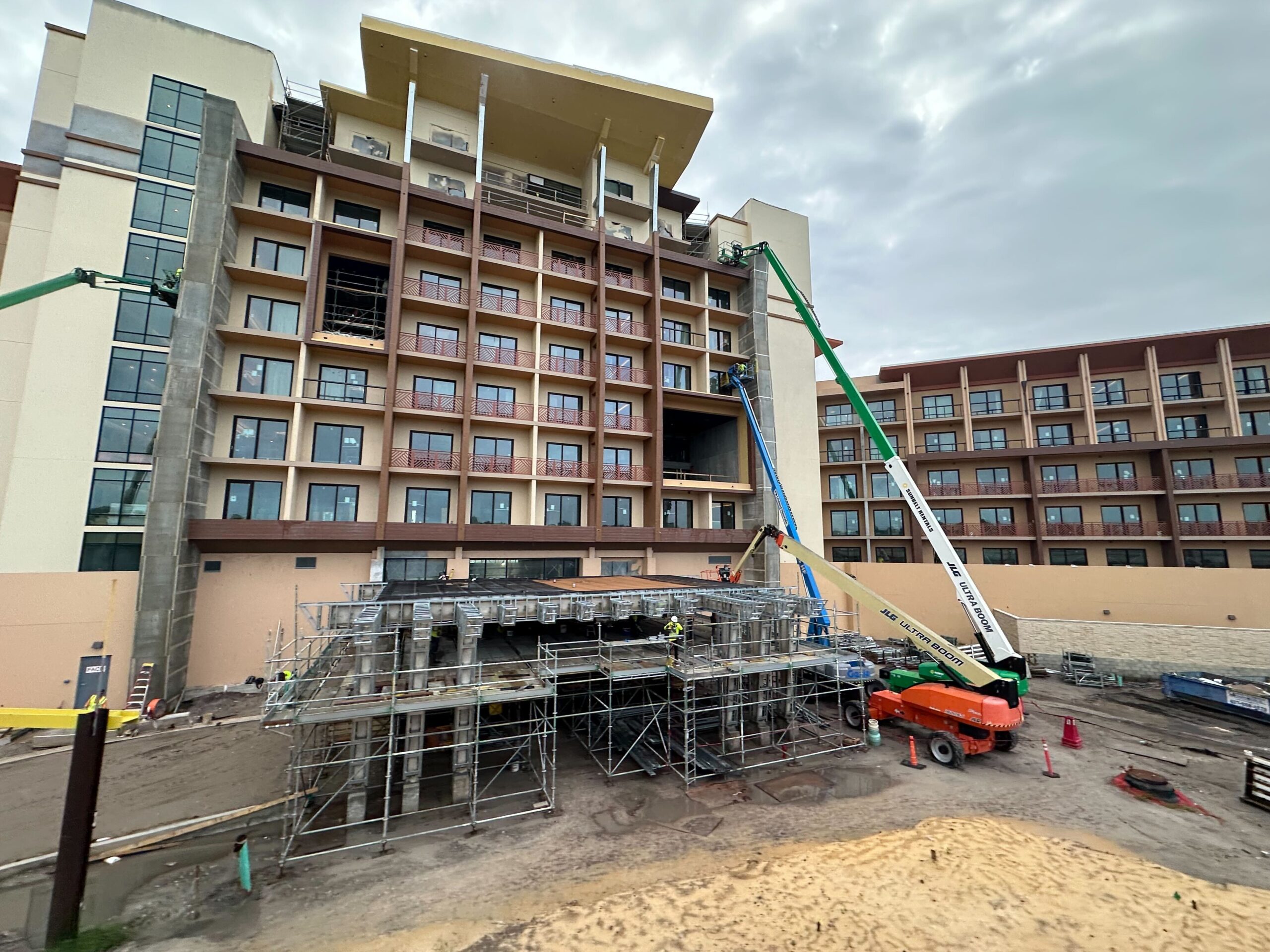 Construction site of a multi-story building with scaffolding and cranes. Workers can be seen on the site performing various tasks.