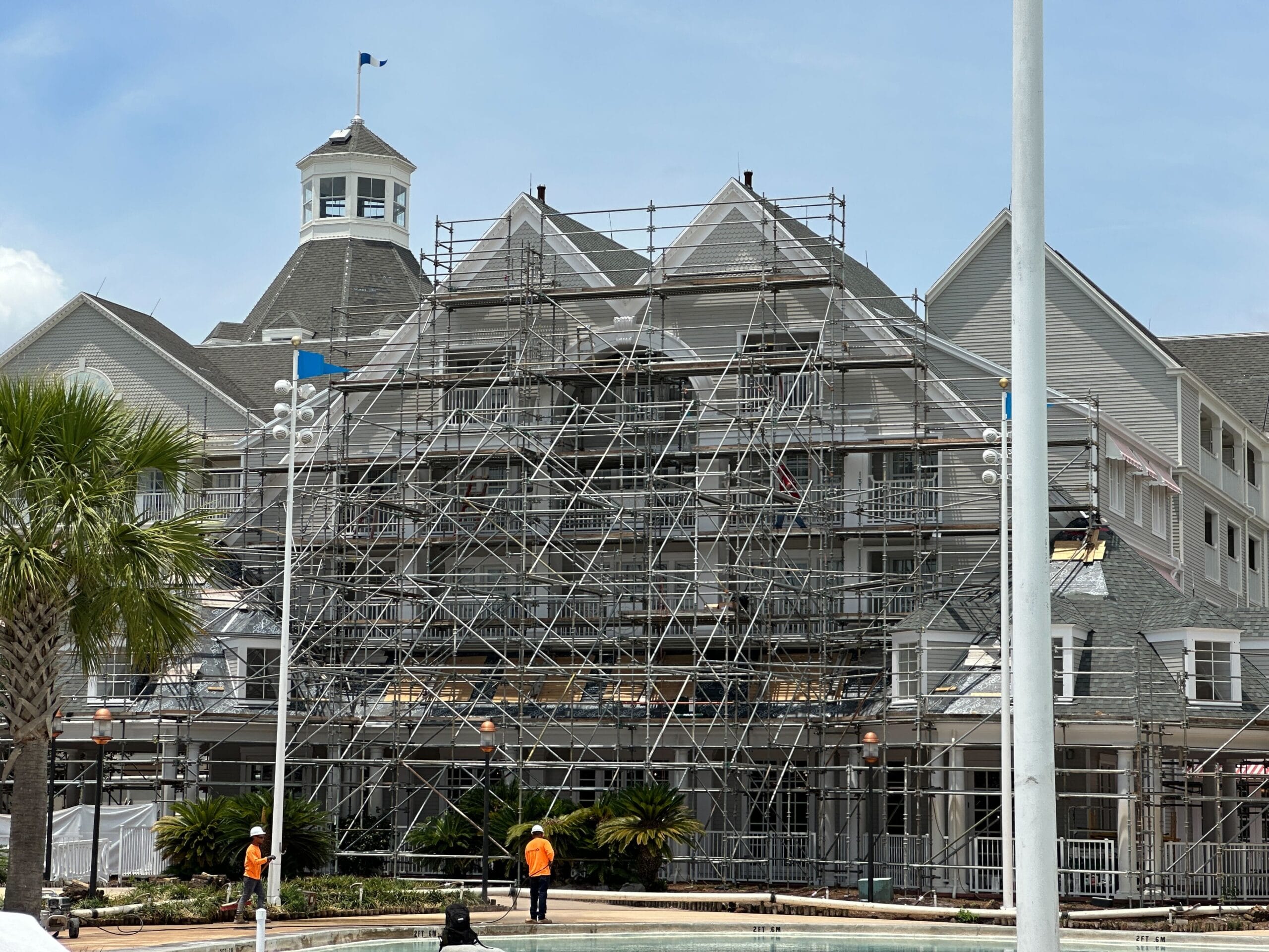 A large building with scaffolding in front, under renovation, with three workers in orange vests nearby.