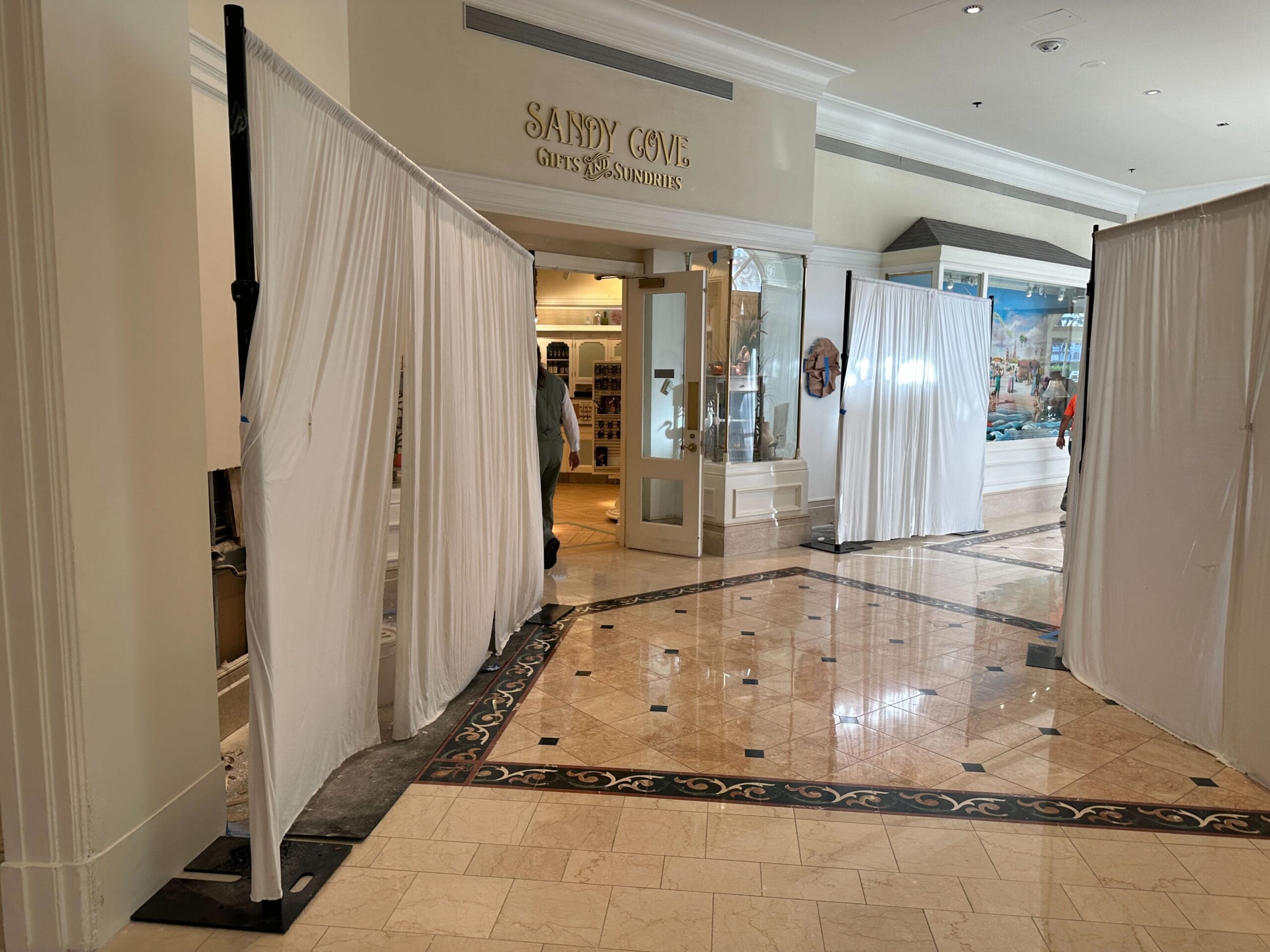White curtains section off part of a shopping mall hallway near the Sandy Cove Gifts & Sundries store entrance.