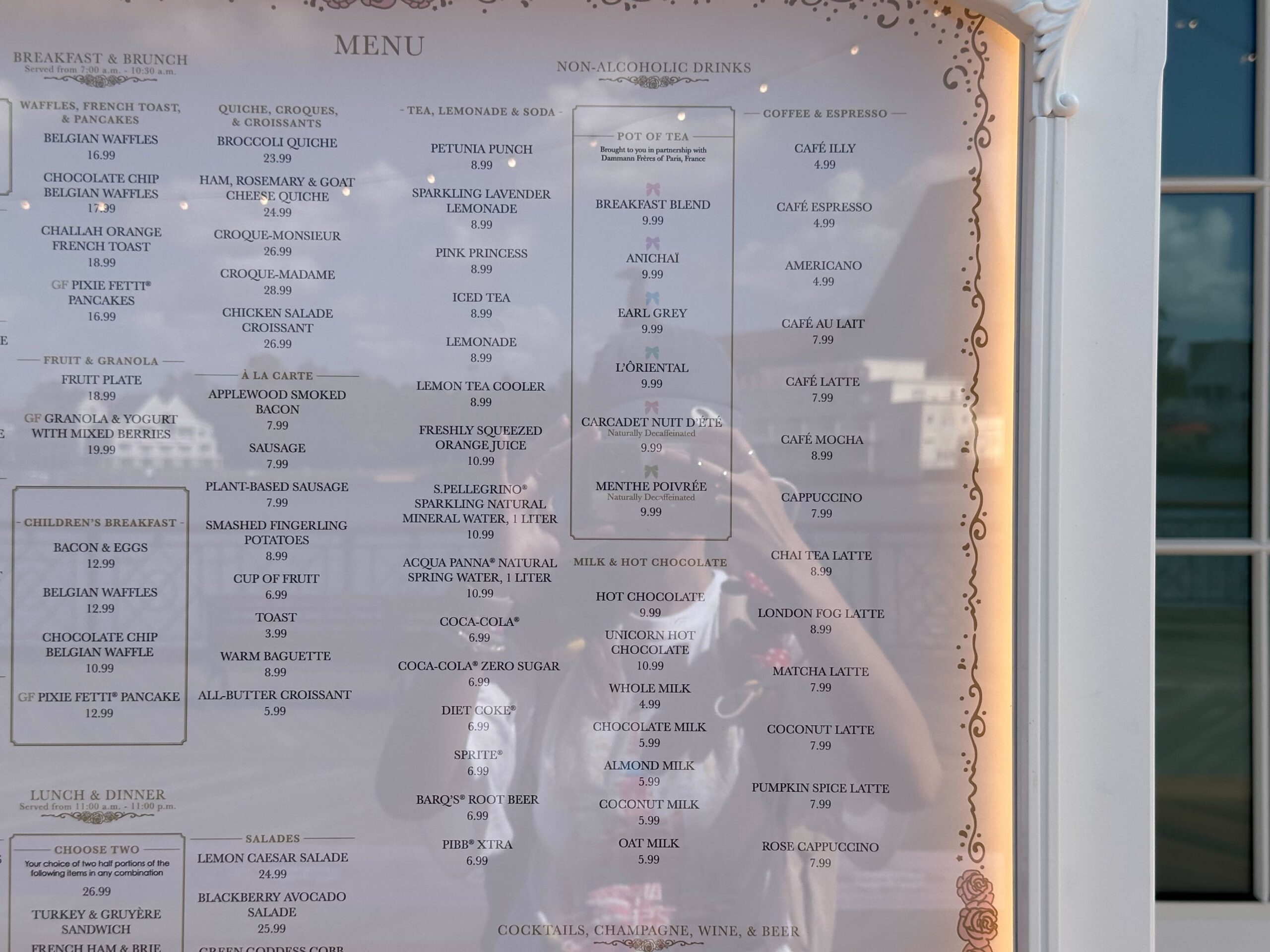 The restaurant menu displayed on the window features breakfast, brunch, lunch, dinner options, and non-alcoholic drinks. Reminiscent of a cake bake shop, the background shows a faint reflection and an inviting outdoor scene.