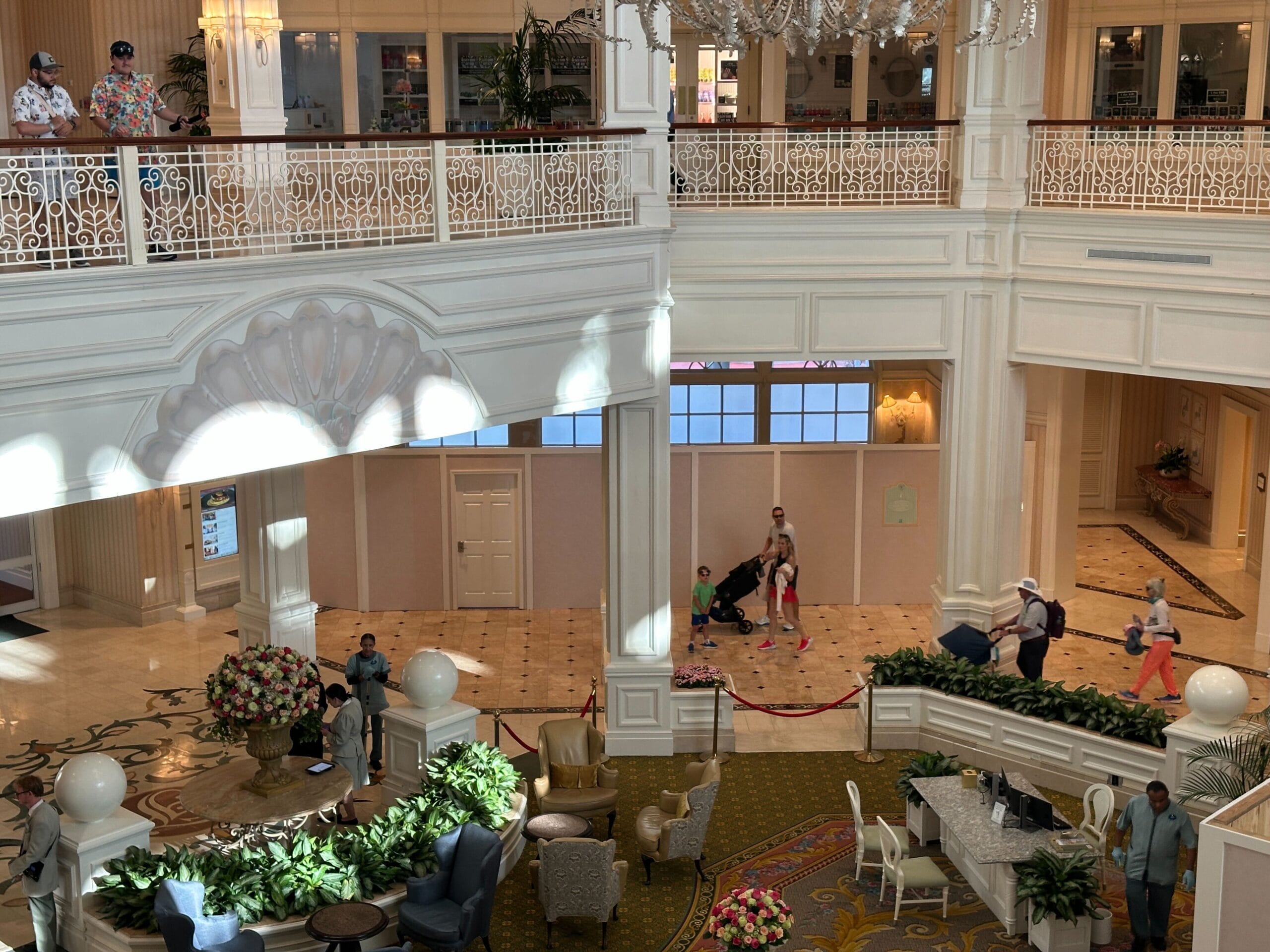 Spacious hotel lobby with people walking, elegant decor, and H2O Glow After Hours food delights amid sunlight and flowers.