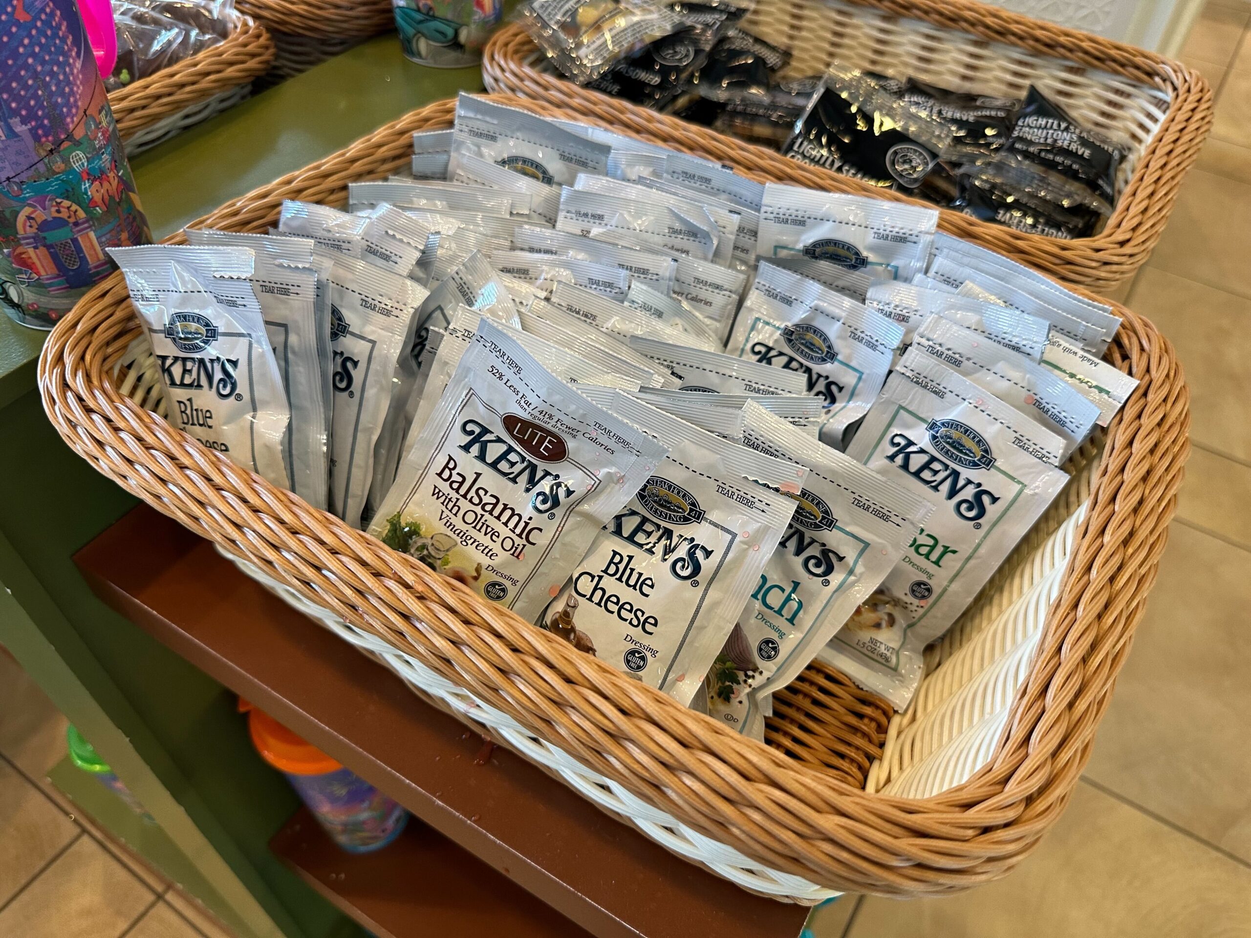 A basket filled with various flavors of Ken's salad dressing packets, including blue cheese, balsamic, and ranch, displayed on a counter.