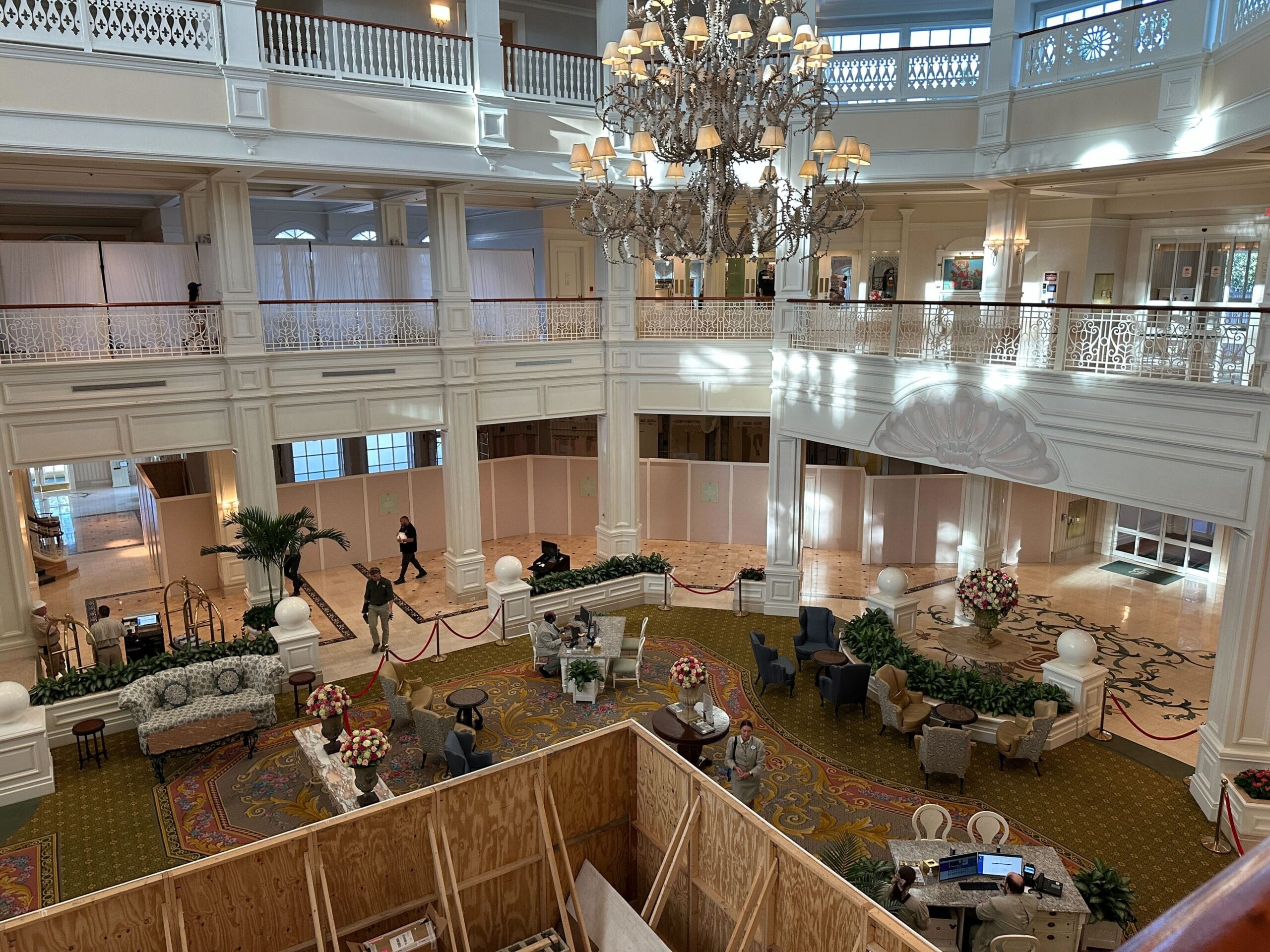 Spacious hotel lobby with elegant decor, chandelier, and construction area partitioned by wooden panels in foreground.