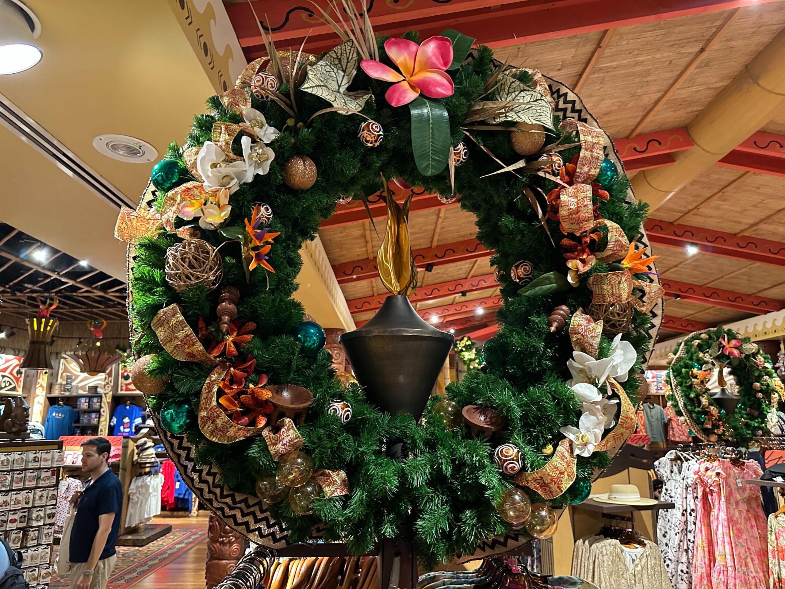 A large decorative wreath with flowers and ribbons is displayed indoors, with store merchandise and a visible shopper in the background.