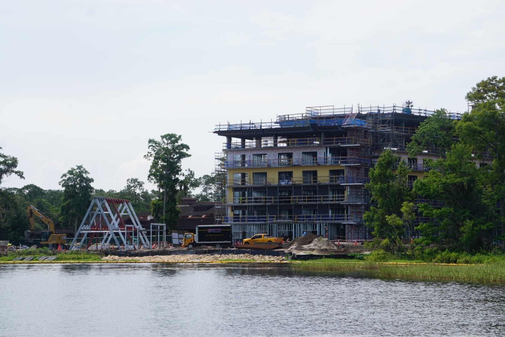 A multi-story building under construction near a lake, with vehicles and equipment visible on the site.