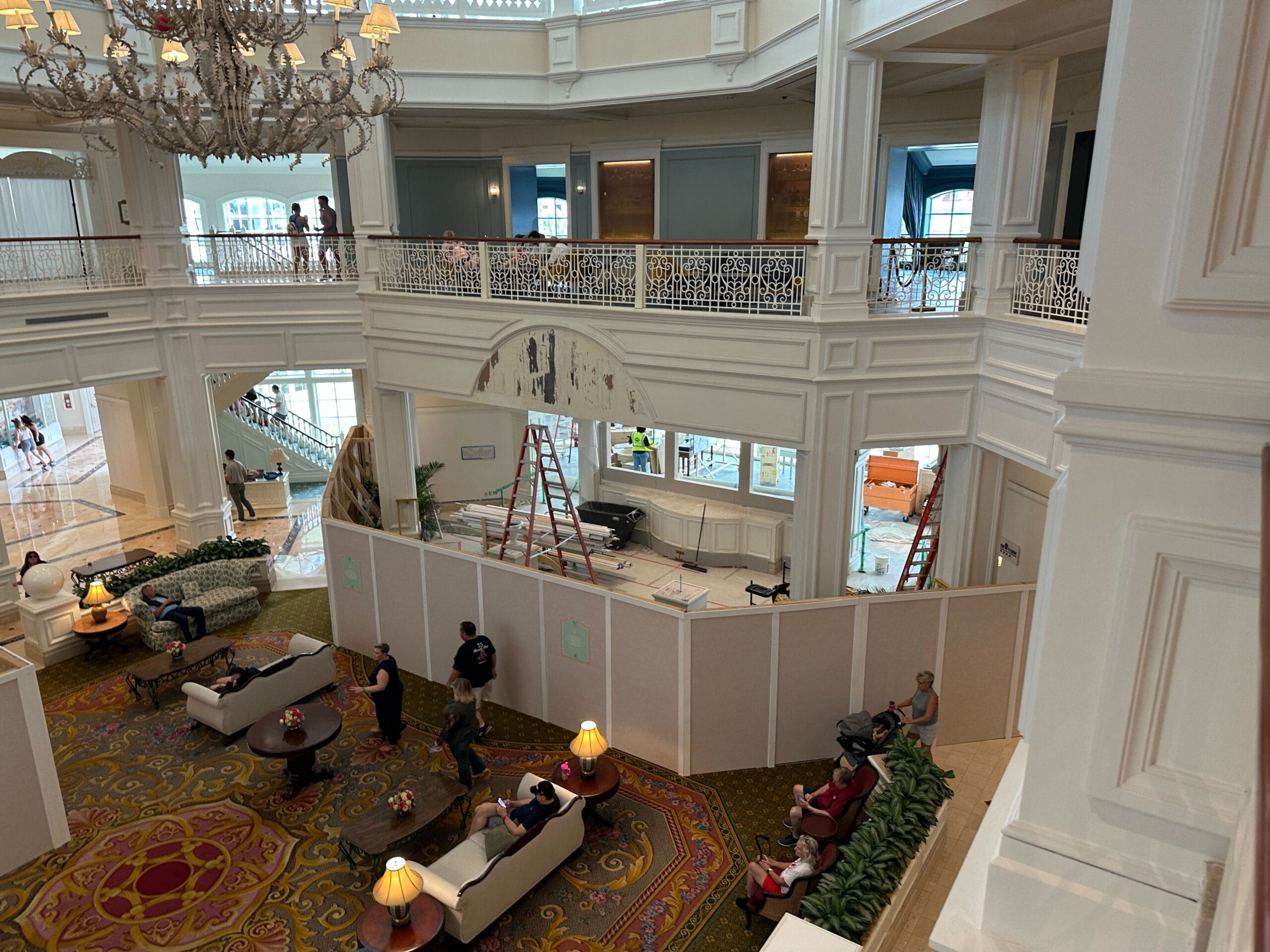 Elegant Grand Floridian Resort lobby with guests, chandeliers, and a fenced construction area with ladders and equipment.