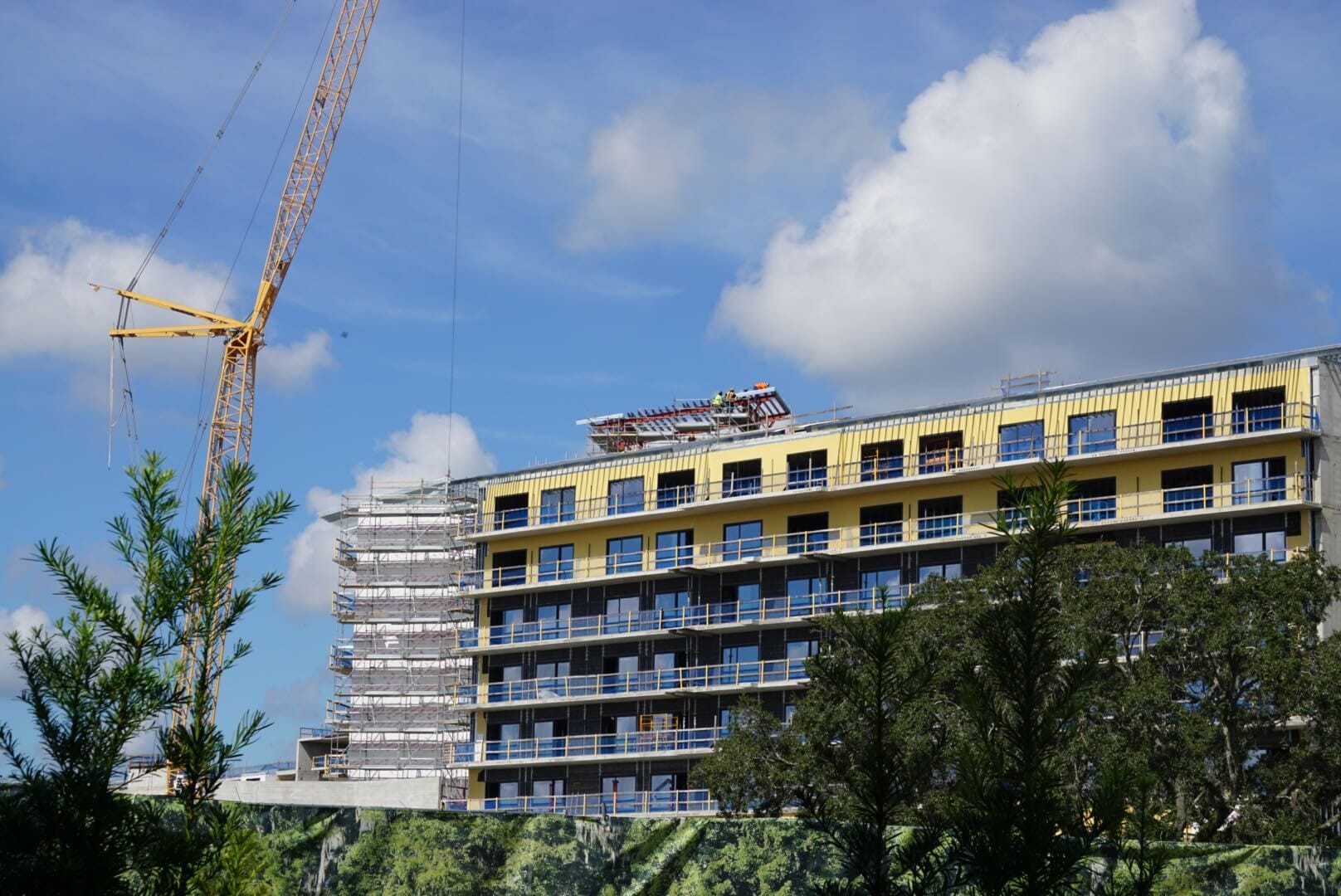 A mid-rise building for Disney Lakeshore Lodge under construction with scaffolding and a yellow crane against a partly cloudy sky.