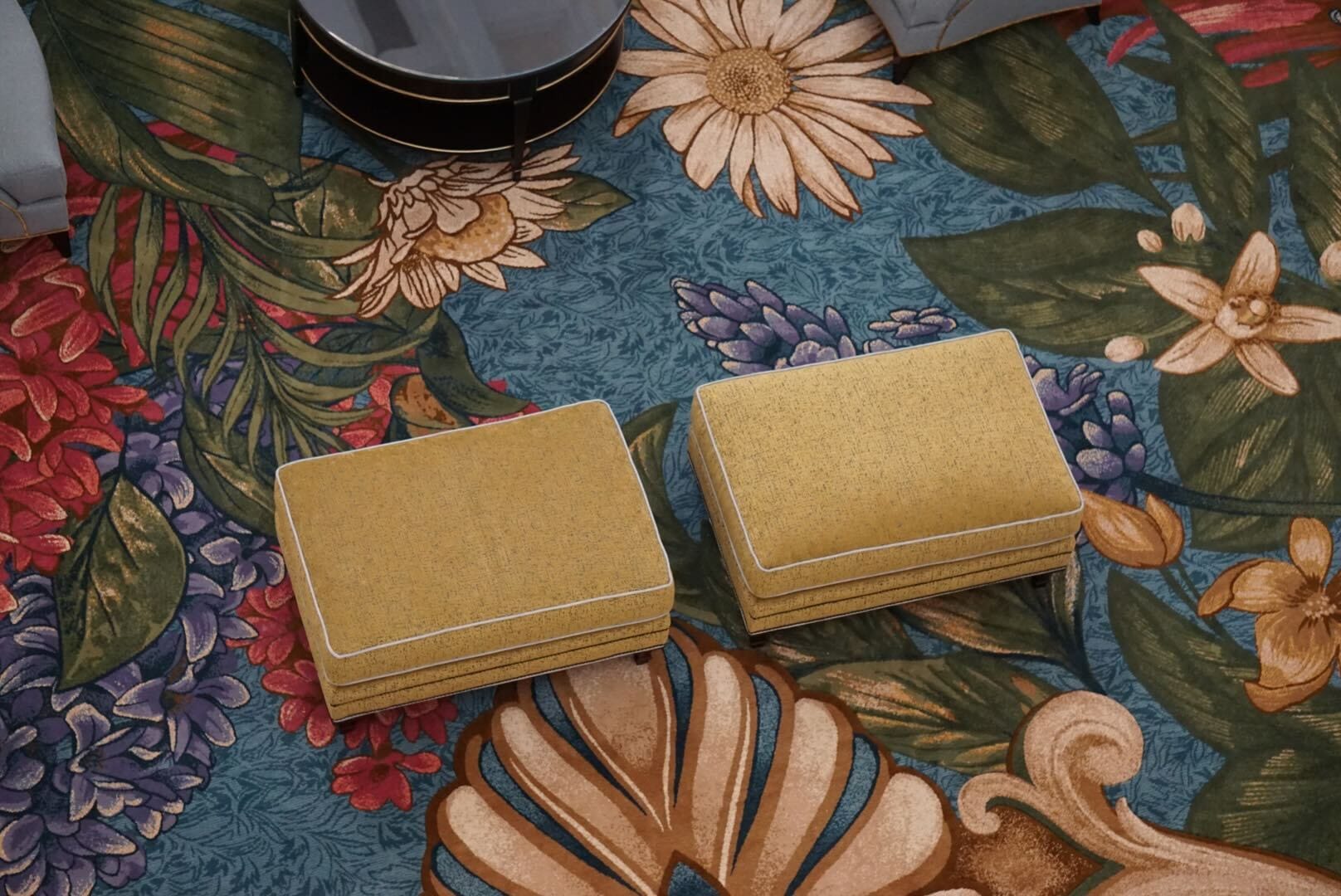 Two yellow ottomans, reminiscent of Disney's Grand Floridian Resort lobby, rest on a floral rug, echoing upscale Disney décor.