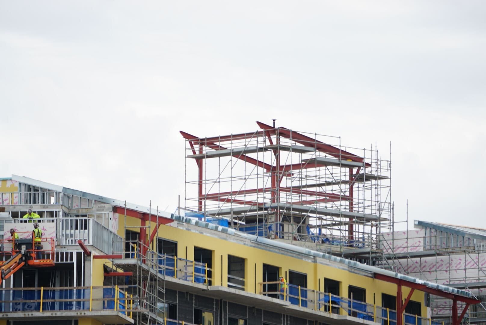 Lakeshore Update: Partially constructed building with scaffolding, exposed steel beams, and workers on an orange lift.
