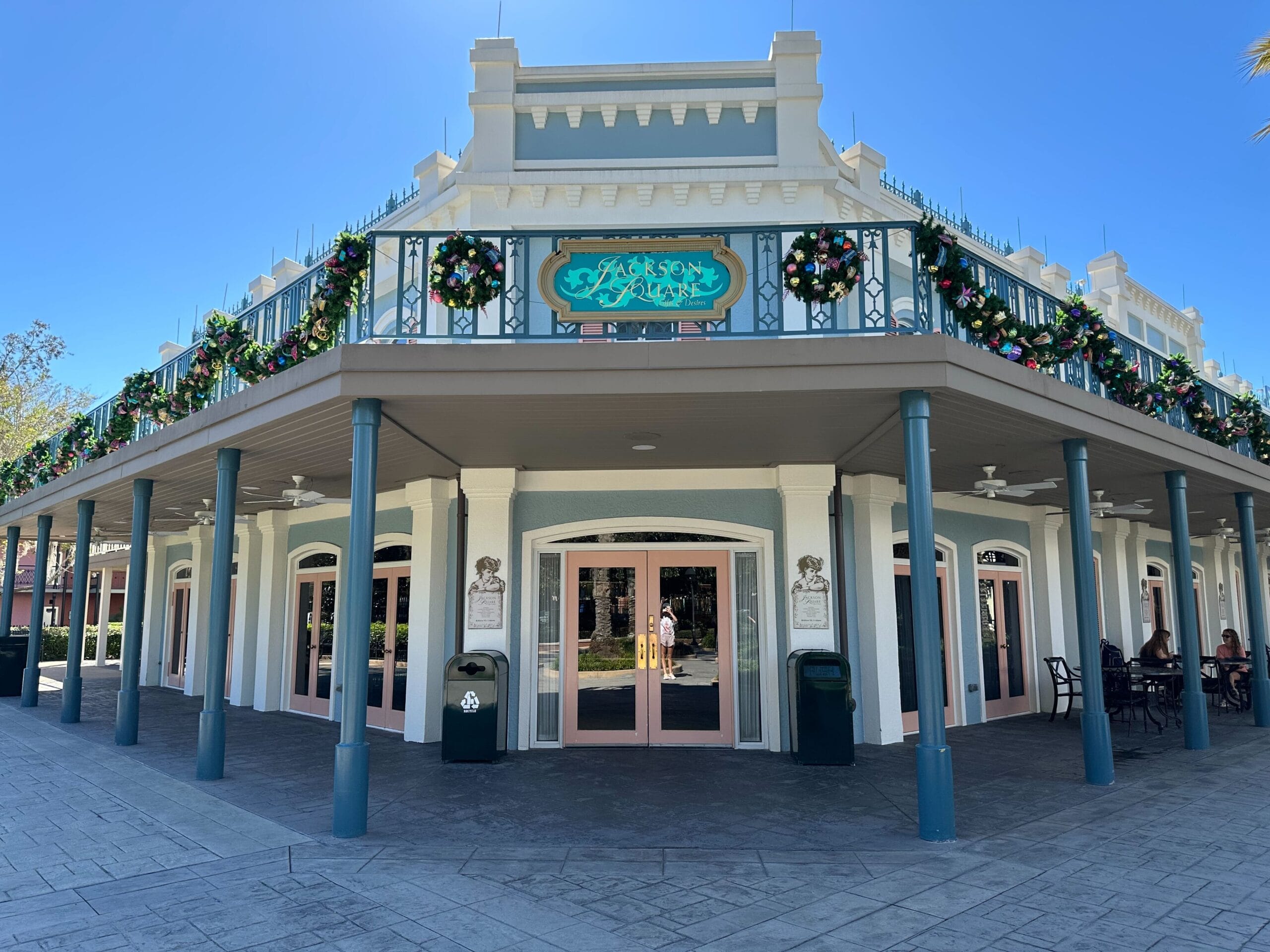 A two-story building with a balcony, decorated with festive wreaths and garlands. The structure has pastel blue and white accents and several arched windows.