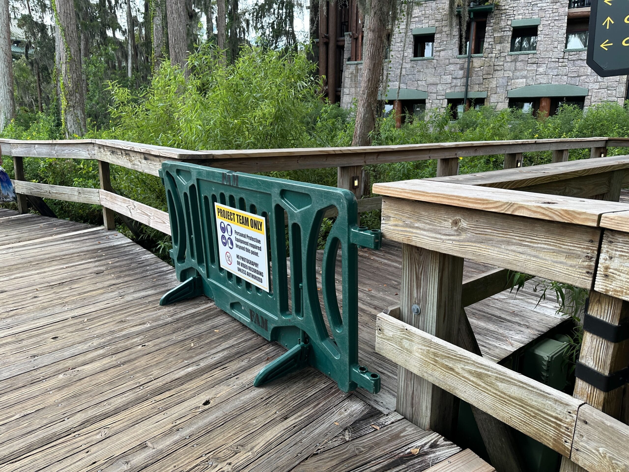 A green barrier blocks a wooden walkway, with a sign indicating that the trail ahead is closed.