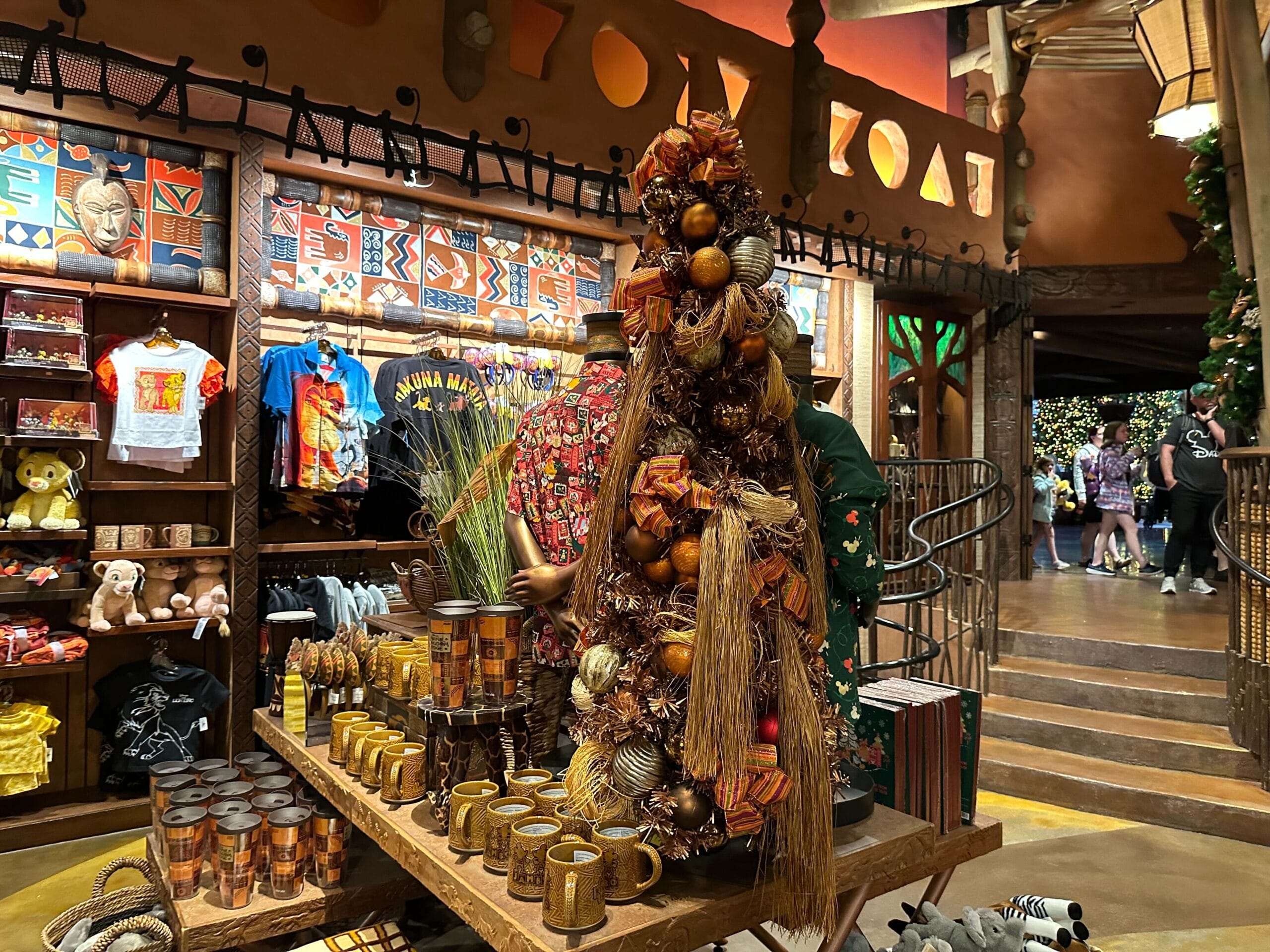 A display inside a store features a mannequin dressed in a fall-themed outfit with assorted decorations. Shelves around it hold T-shirts, mugs, and various merchandise.