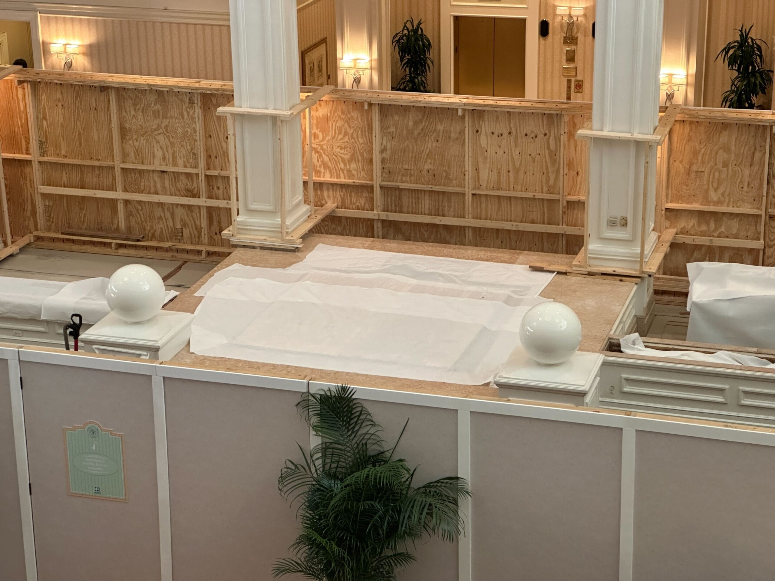 Wooden construction barriers with white coverings and potted plants inside a large, elegant indoor space.
