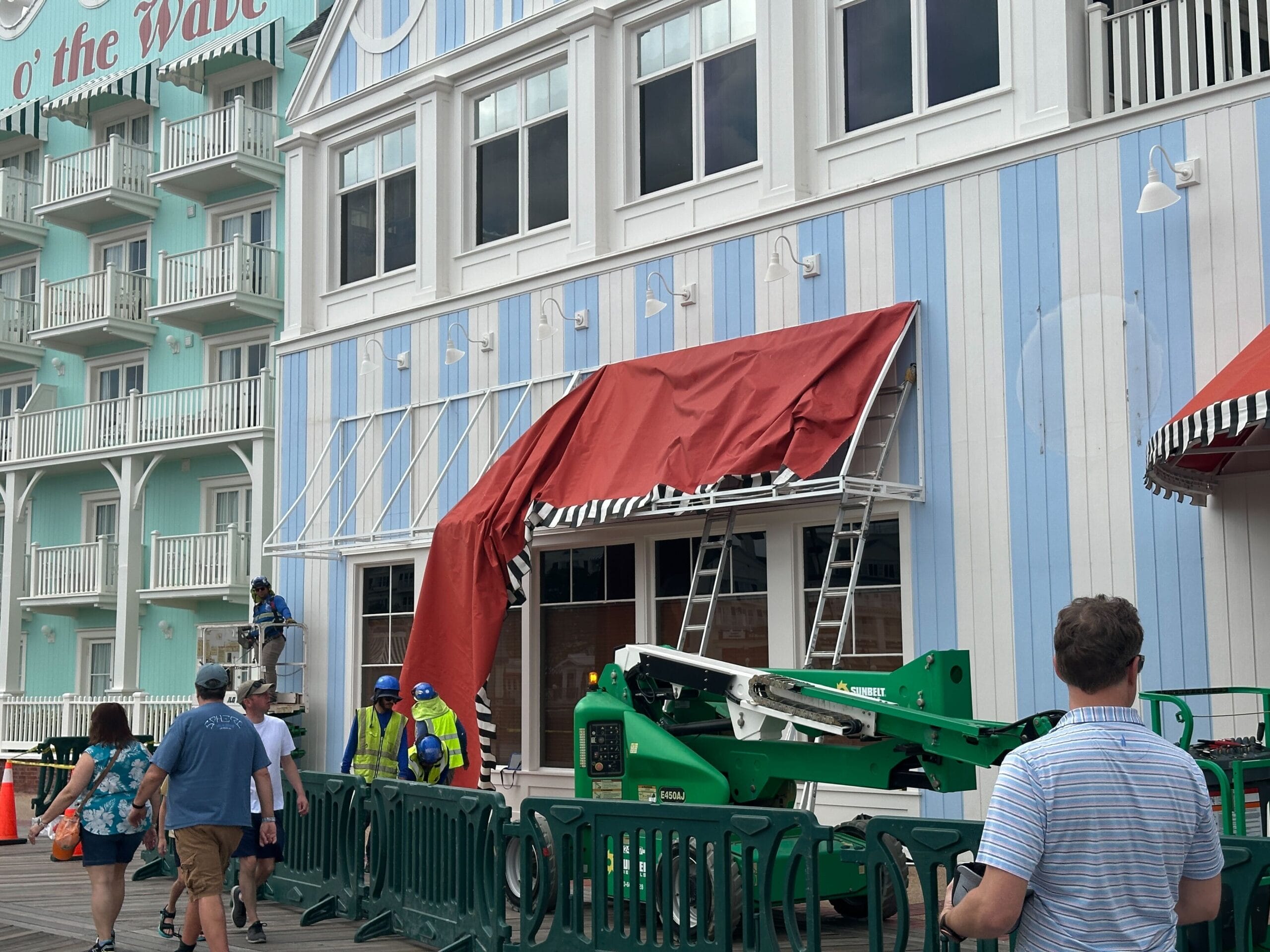 Workers install a red Jellyrolls Awnings canopy on a blue-and-white striped building along Disney's BoardWalk.