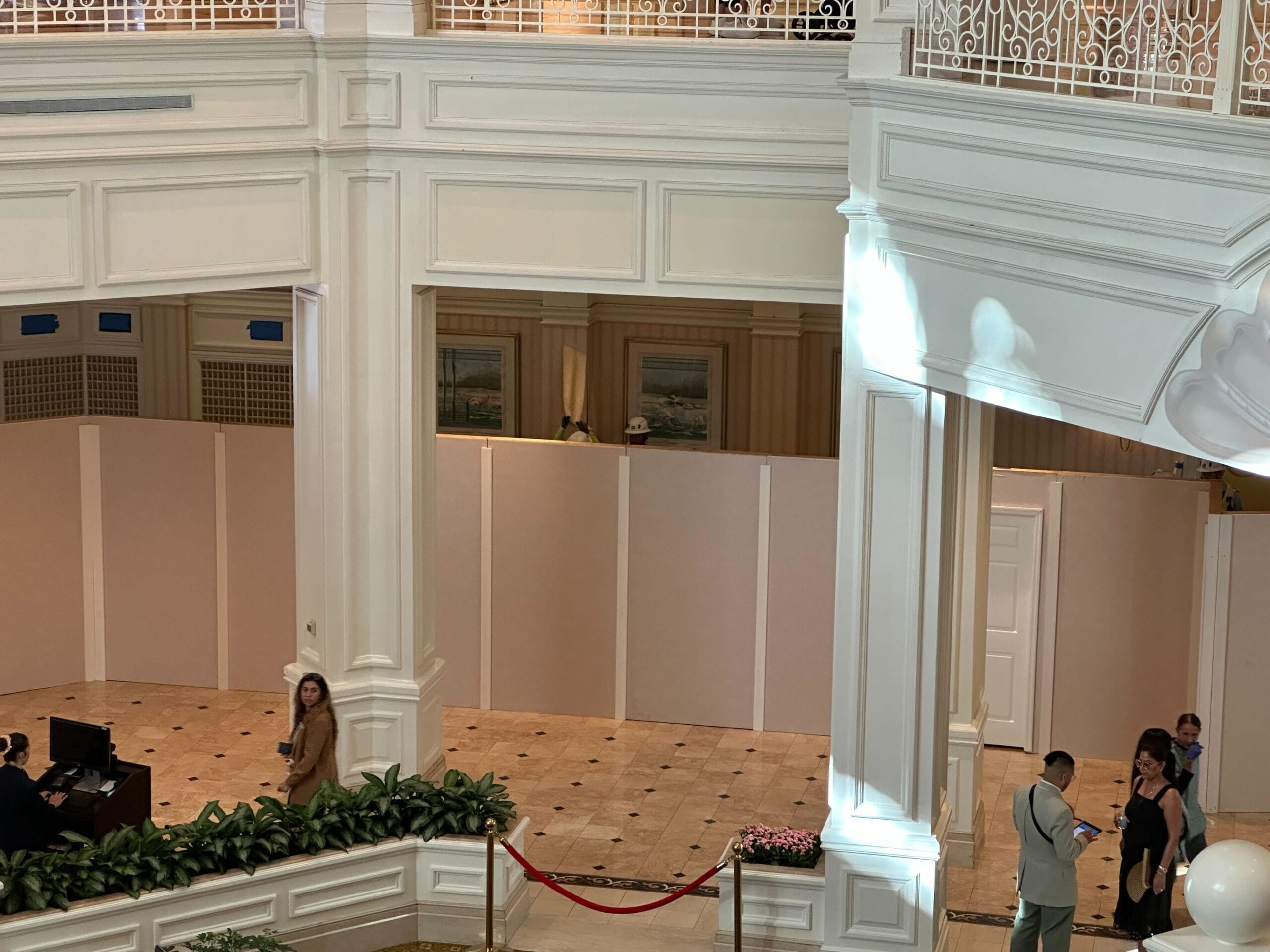 A white construction wall in a hotel lobby, with people standing and talking nearby.