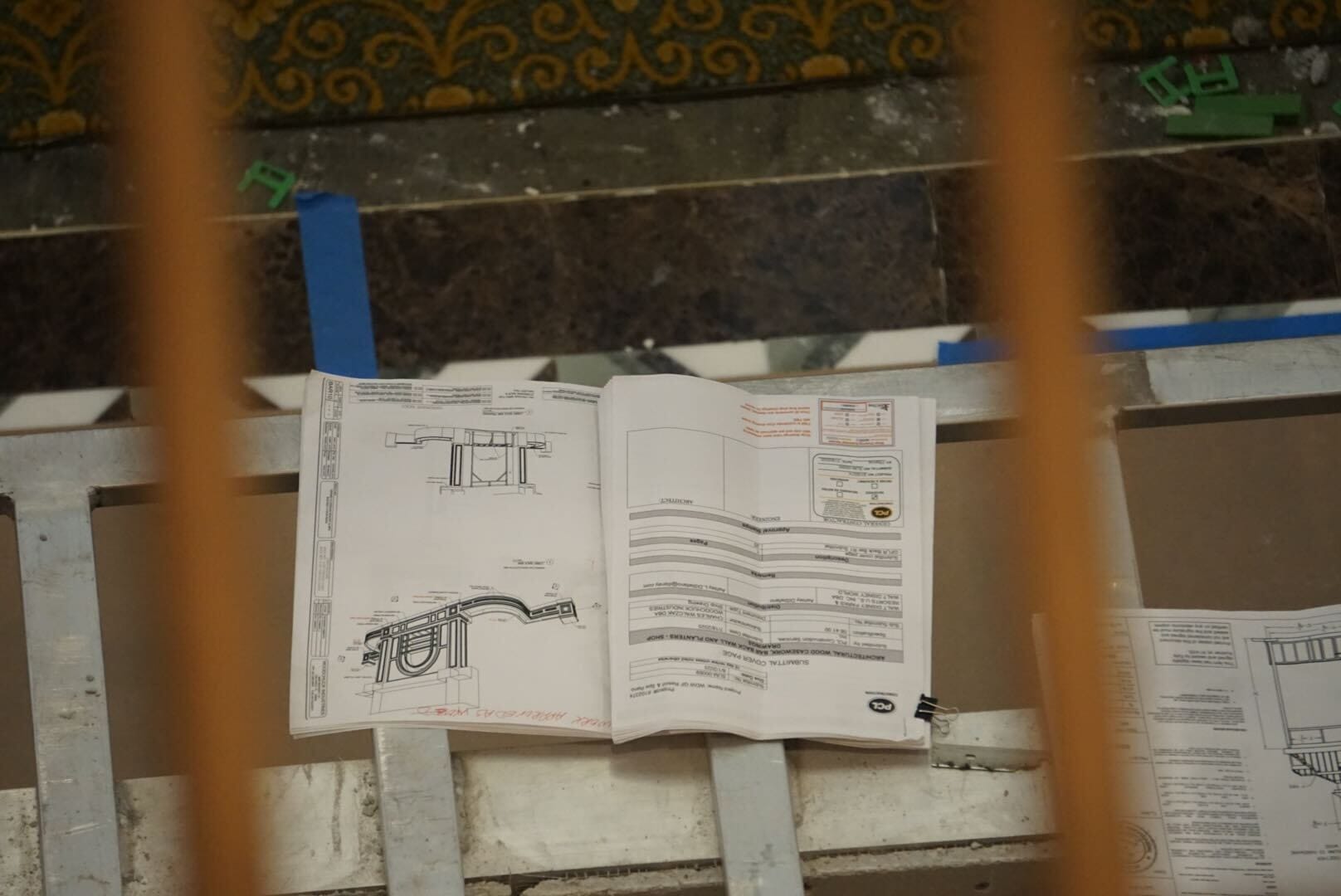 An open technical manual with diagrams and text sits on a metal railing, viewed through vertical bars.