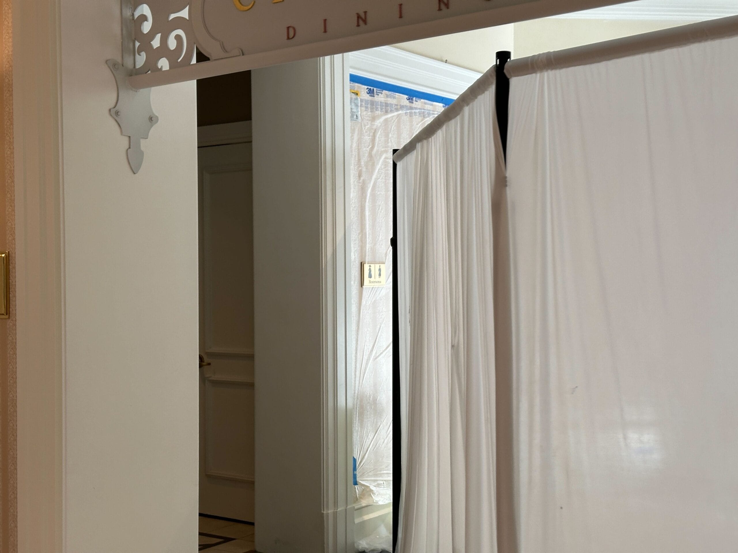 White curtains block off a hallway near a partially visible door and an ornate sign with the word DINING above.