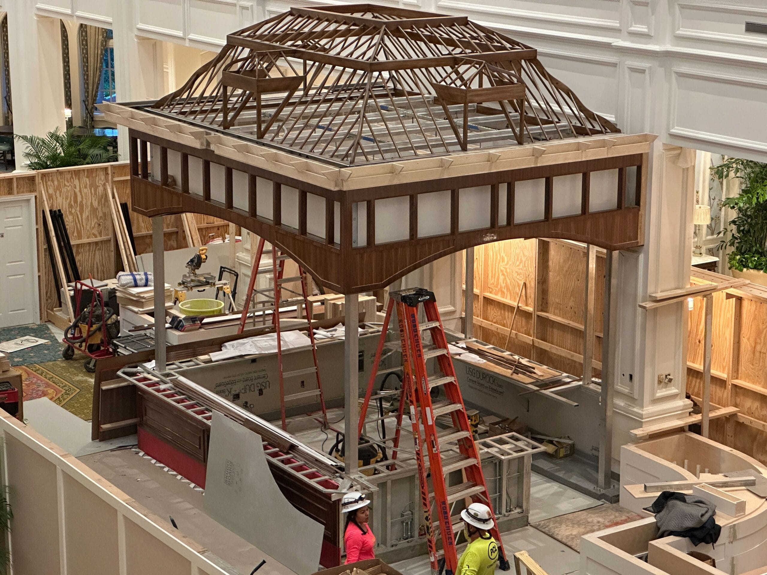 Two construction workers build a large wooden structure inside the partially finished Grand Floridian indoor space.