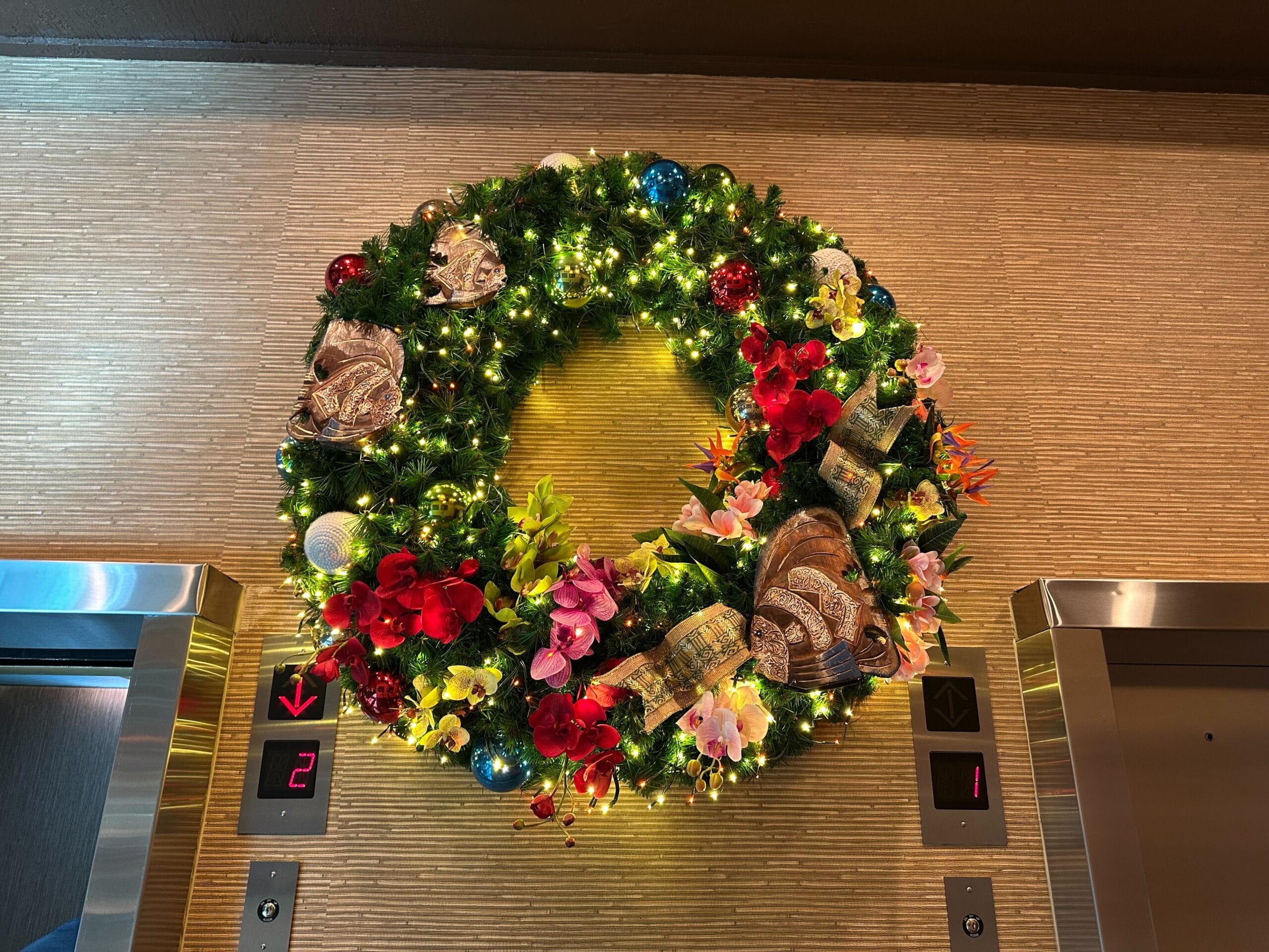 A decorative wreath with lights, flowers, and ornaments hangs above elevator doors.