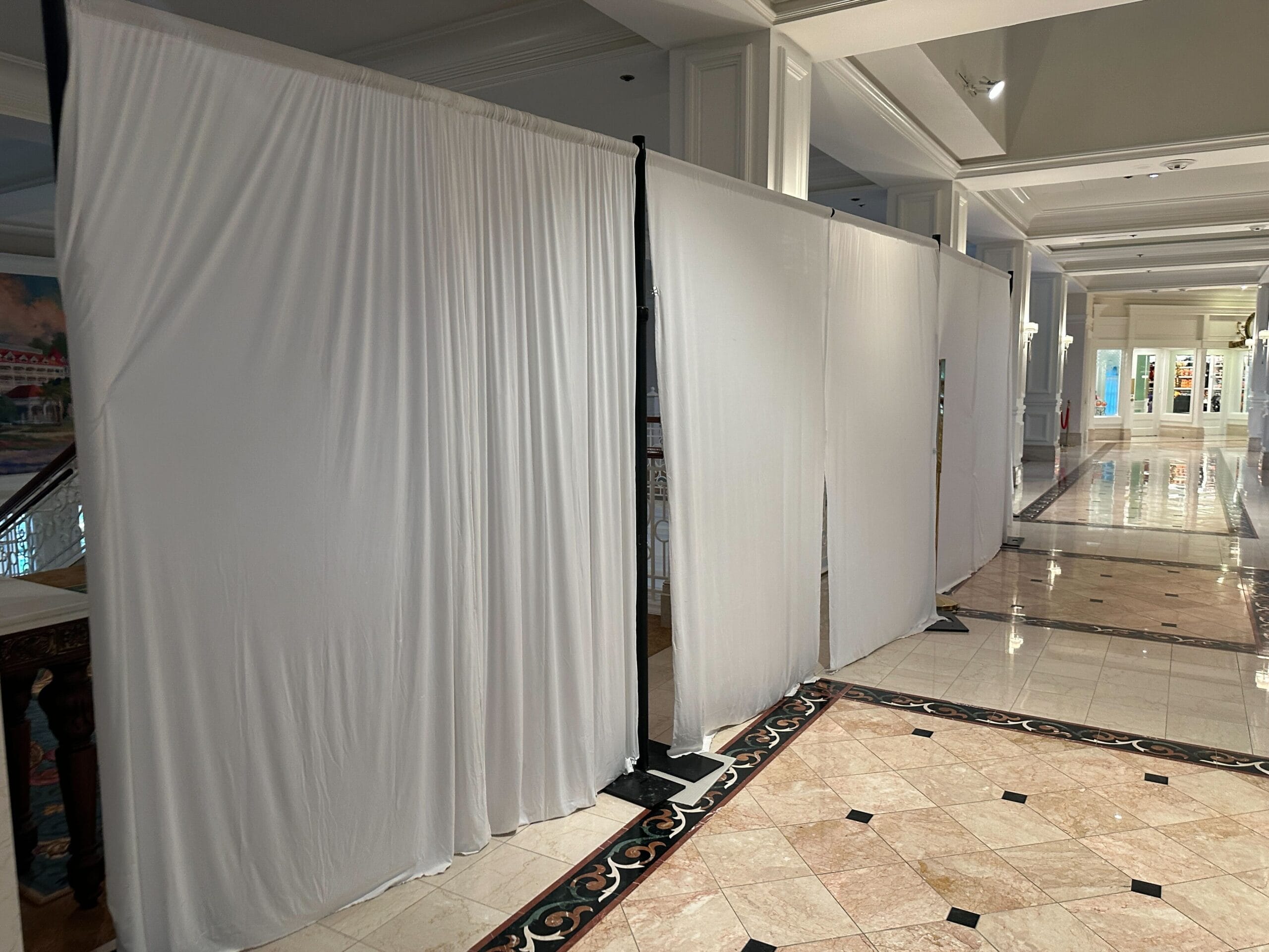 White curtains on metal stands block off an area in a spacious hallway with tiled floors and white walls.