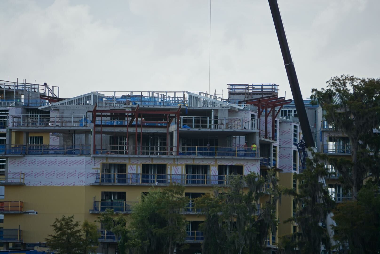 Lakeshore Lodge construction updates: A multi-story building rises with workers, scaffolding, and a crane silhouetted against clouds.