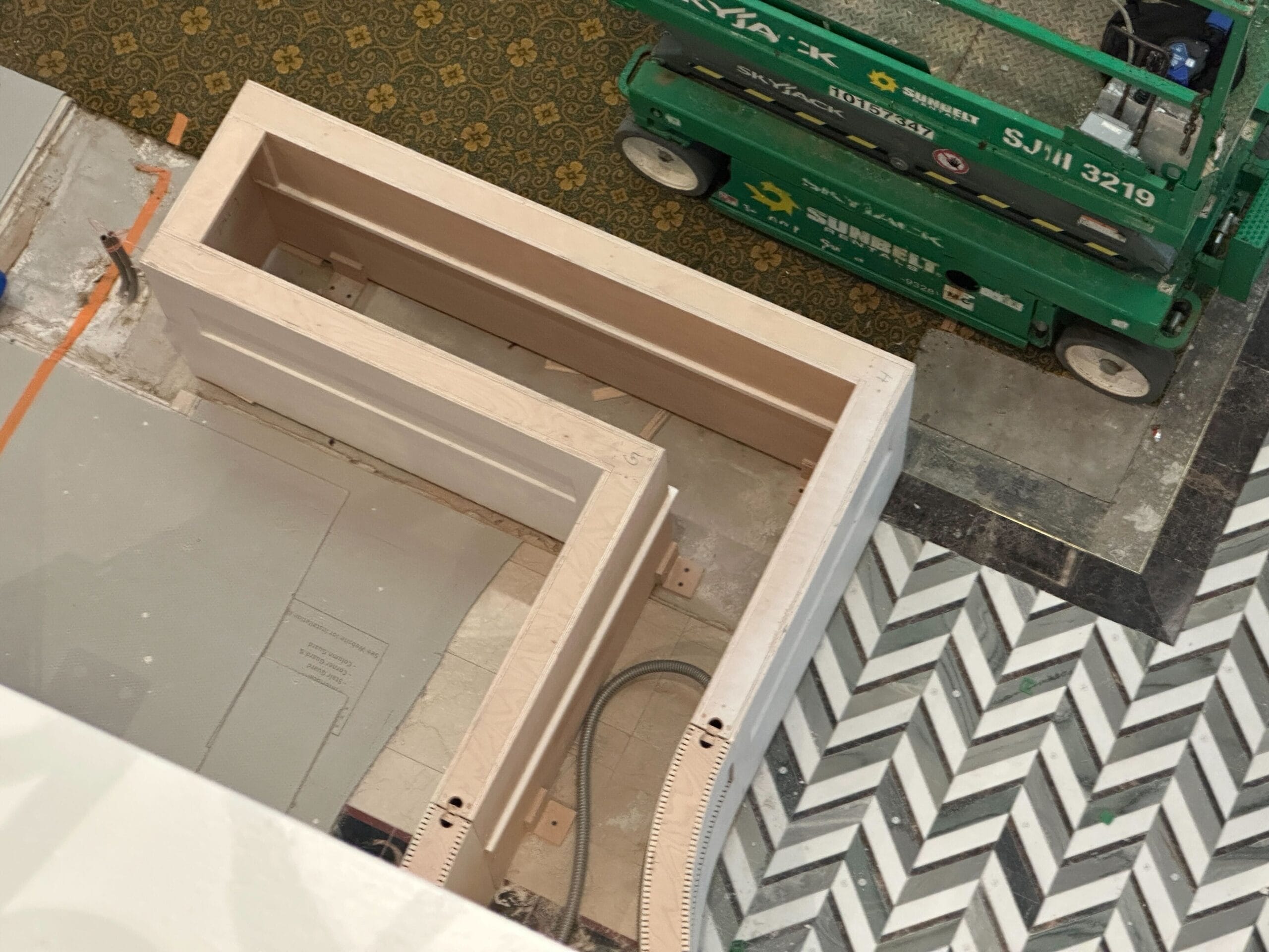 A partially constructed wooden structure near a green lift, surrounded by patterned tiles and Grand Floridian wallpaper.
