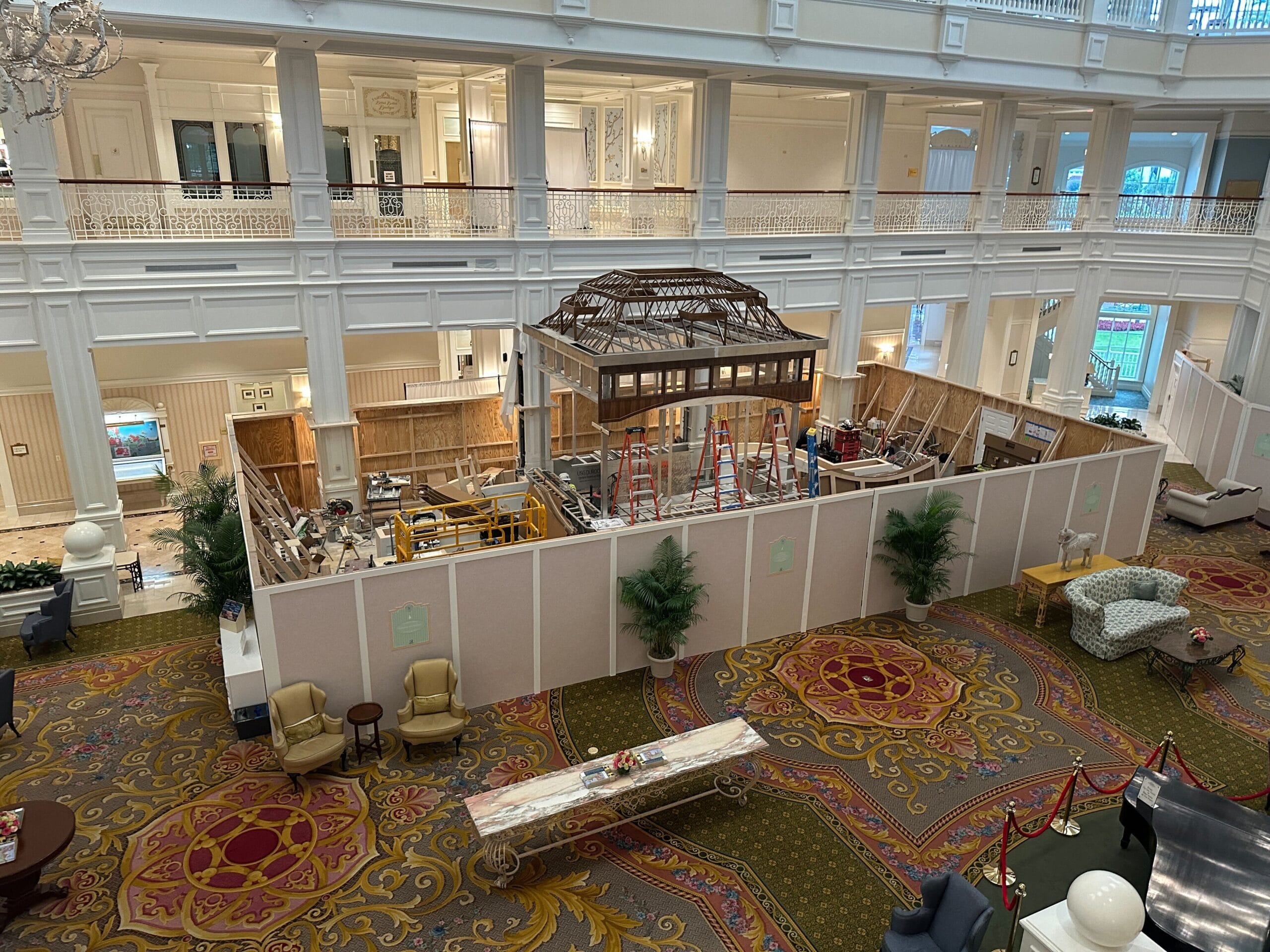 Lobby with ornate carpet, seating areas, and a large construction zone enclosed by barriers in the center.
