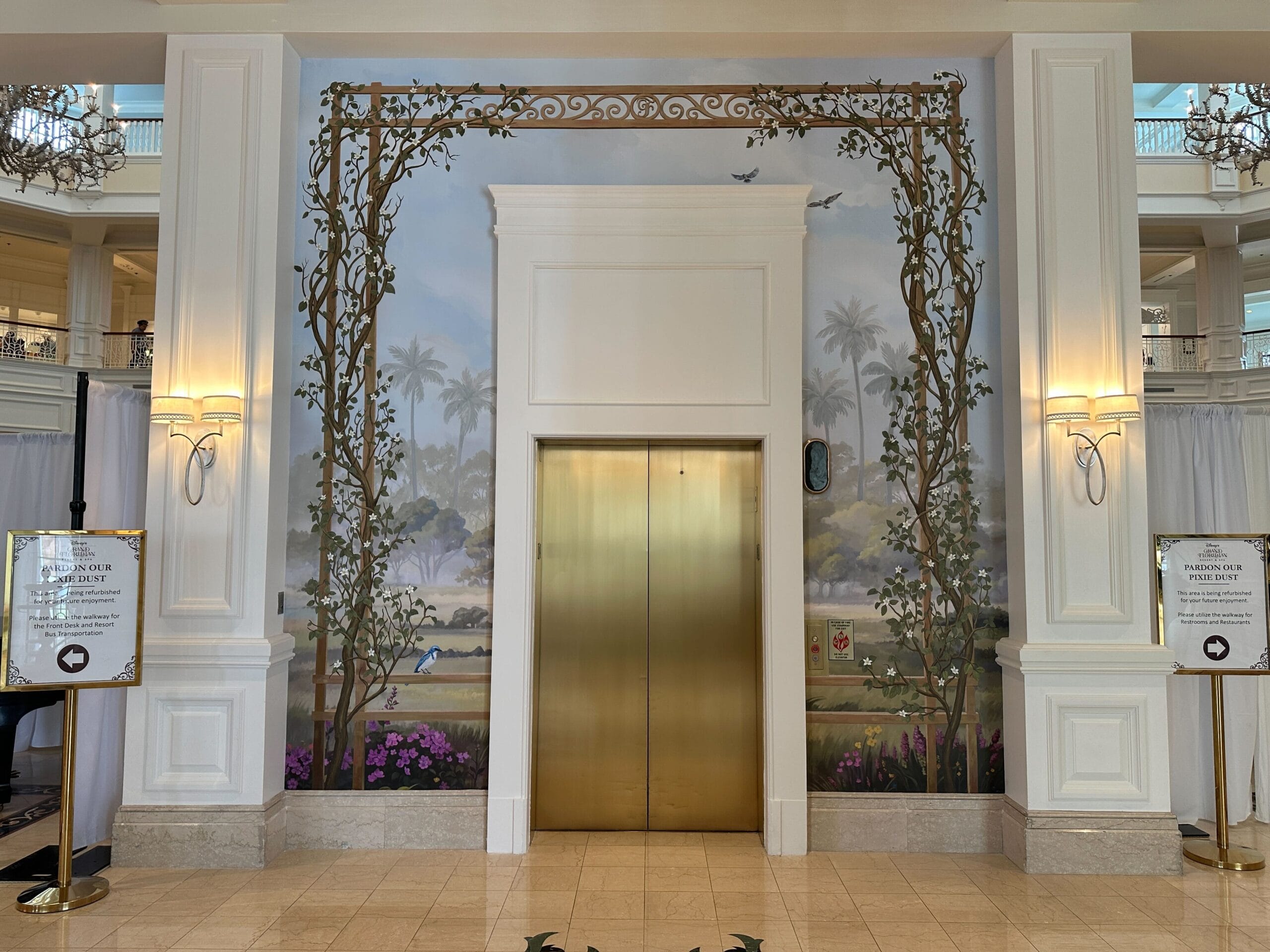 A gold elevator with a floral mural and ornate frame, reminiscent of the luxury style in Disney’s Grand Floridian Resort hotel lobby.