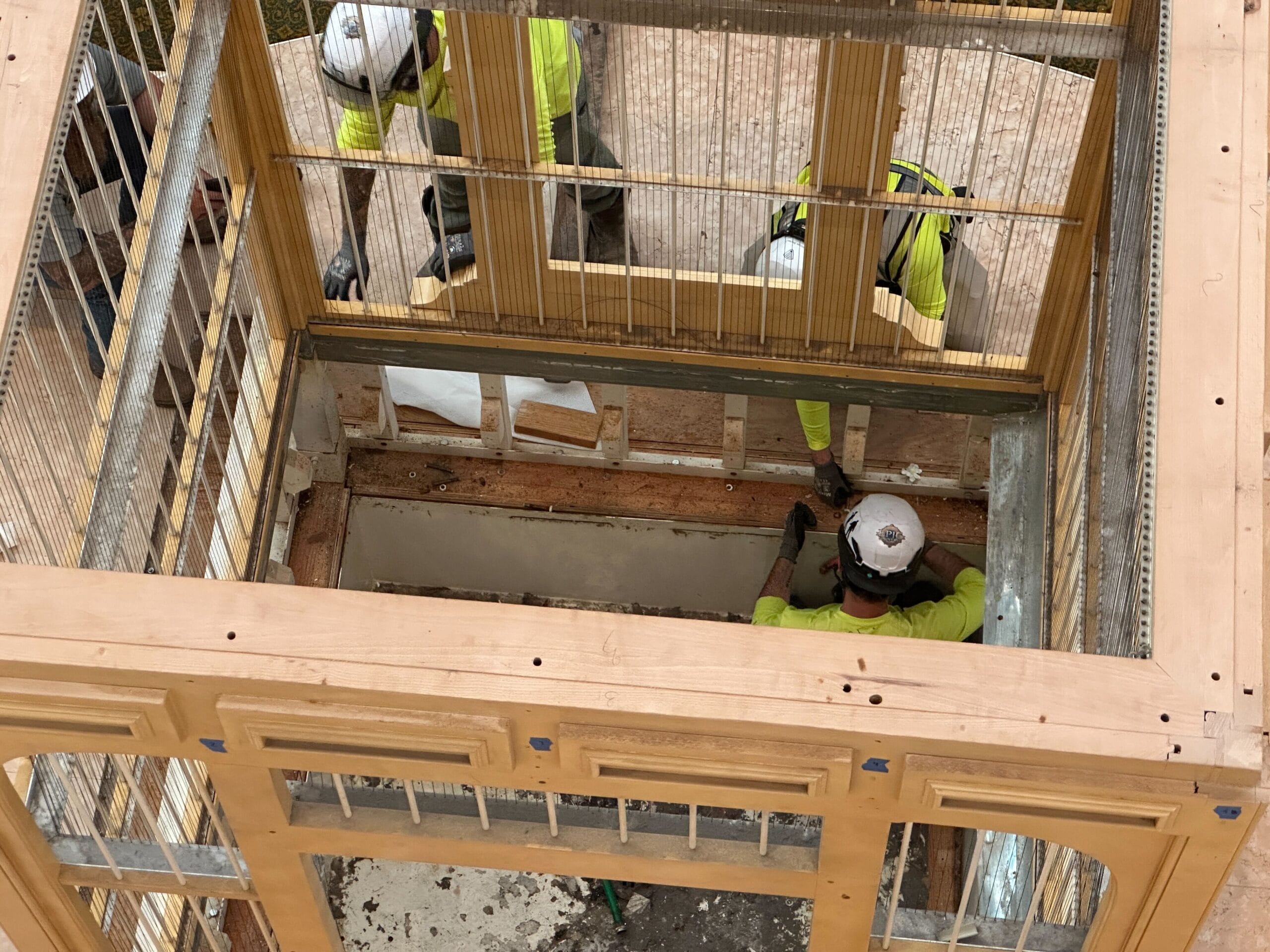 Three construction workers in safety gear remodel a wooden structure during the Grand Floridian Resort lobby upgrade.