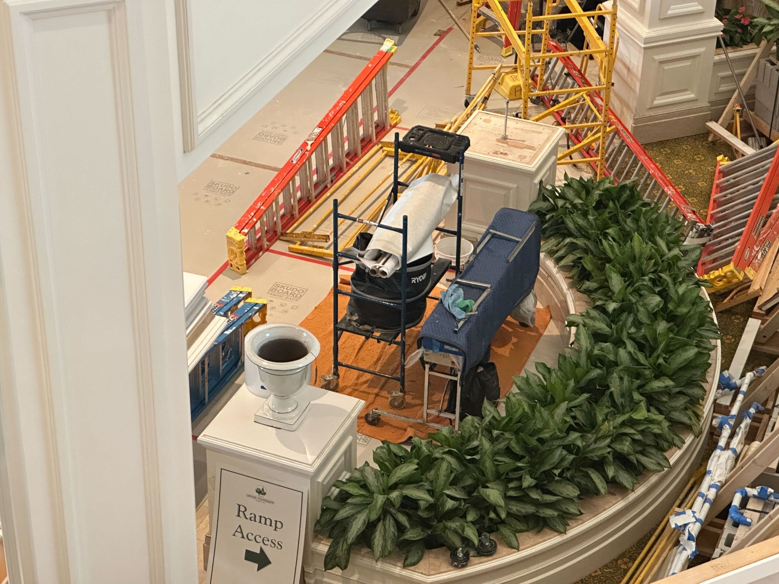 A construction area with ladders, equipment, and barriers near a Ramp Access sign and Grand Floridian wallpaper.