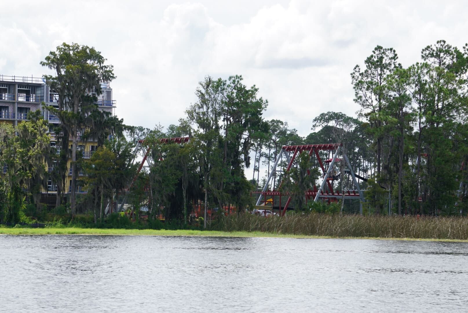 A lakeside view of a hotel and two red swinging amusement park rides partially hidden by trees.