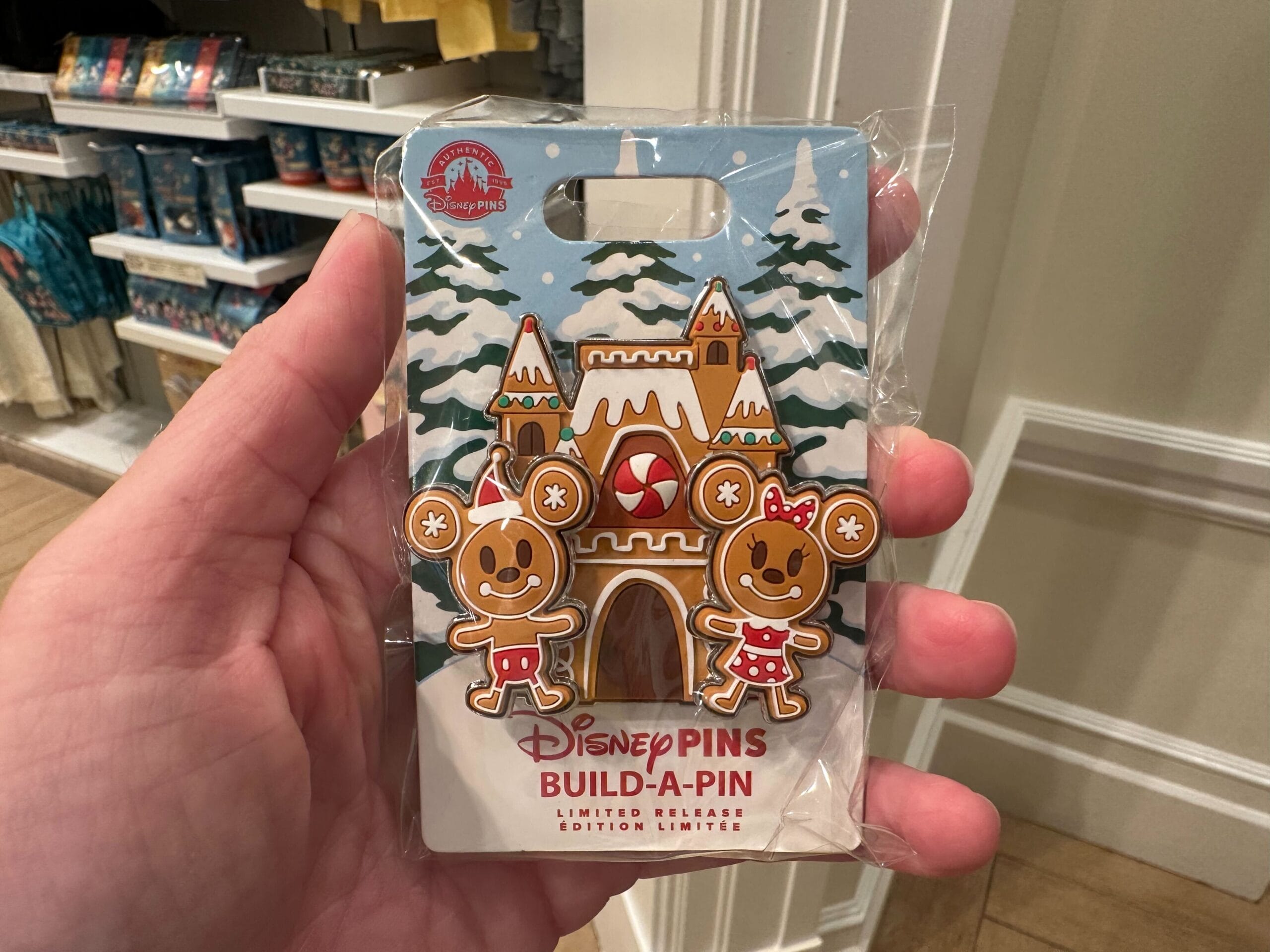 Hand holding a Disney Build-A-Pin featuring a gingerbread castle and two gingerbread characters in festive attire.