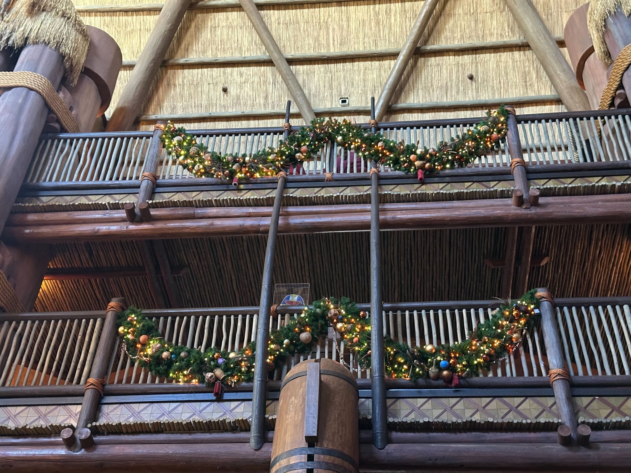 Christmas garlands with lights and ornaments decorate a wooden balcony with a thatched roof above.