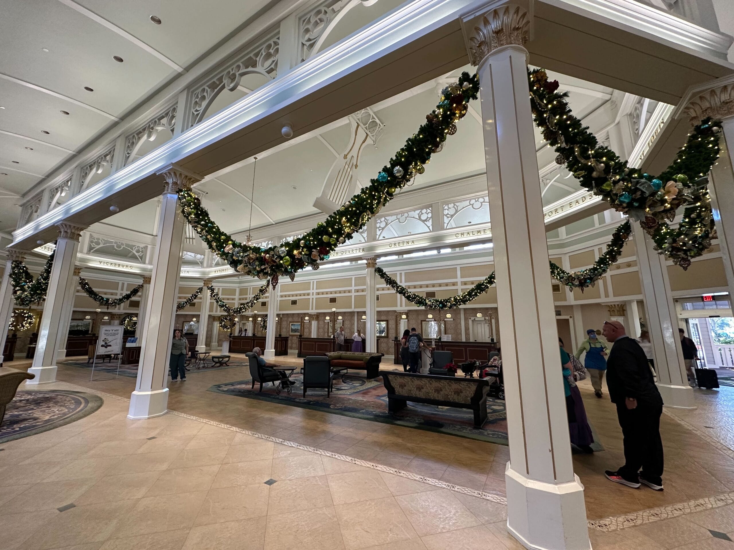 A decorated hotel lobby with festive garlands hanging from the ceiling and columns. People are standing and sitting in the seating area.