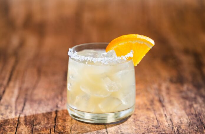 A glass of iced breakfast cocktail with a salted rim and an orange slice garnish sits invitingly on a wooden surface, perfect for a magical start reminiscent of a Walt Disney World morning.