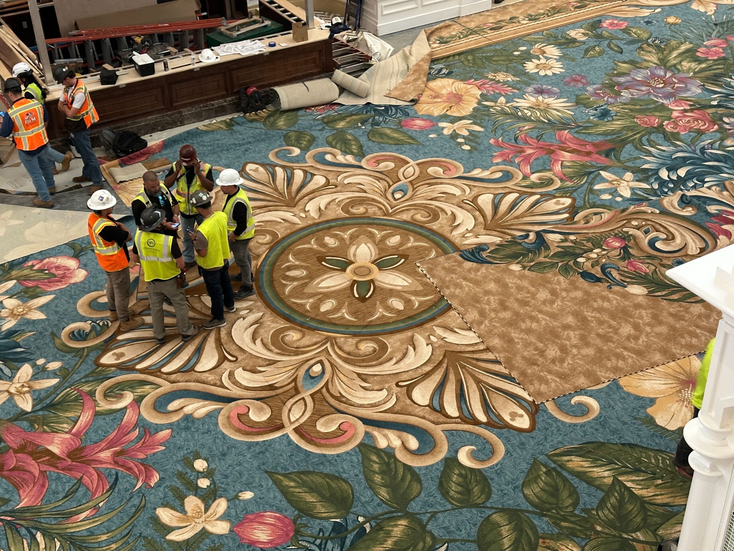 Crew in safety gear works on carpeting in the Grand Floridian Lobby at Walt Disney World, with elegant decor reminiscent of Main Street USA.