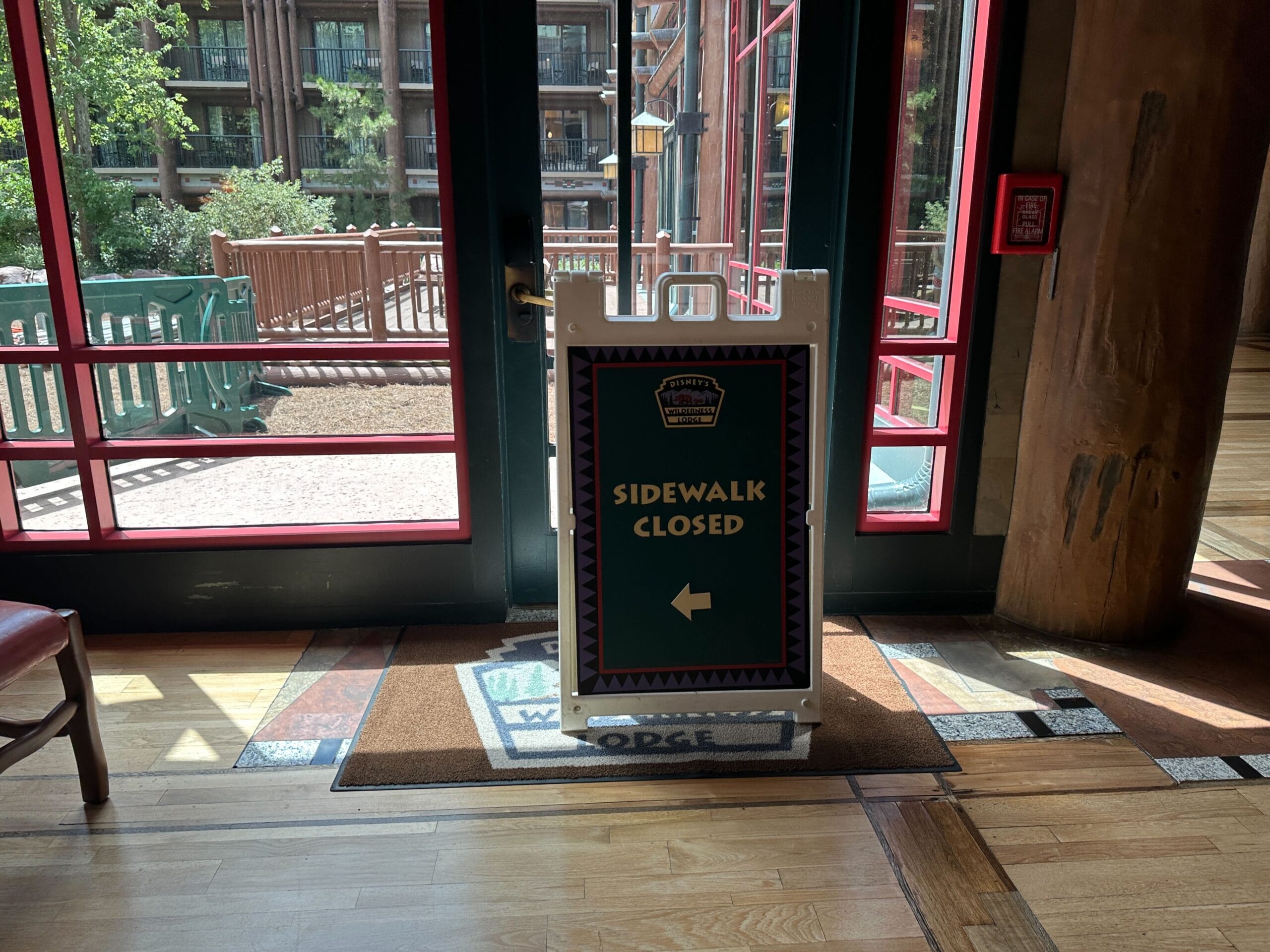 A sign inside a building reads Sidewalk Closed with a left arrow, blocking a glass door to the outside.