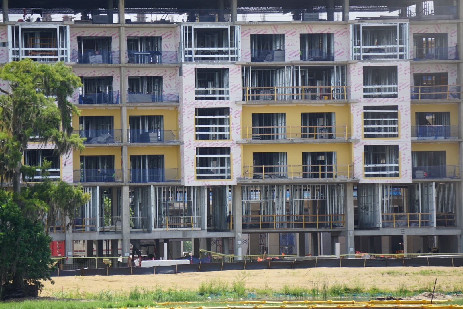A multi-story building under construction with exposed framing, windows, and yellow insulation panels.