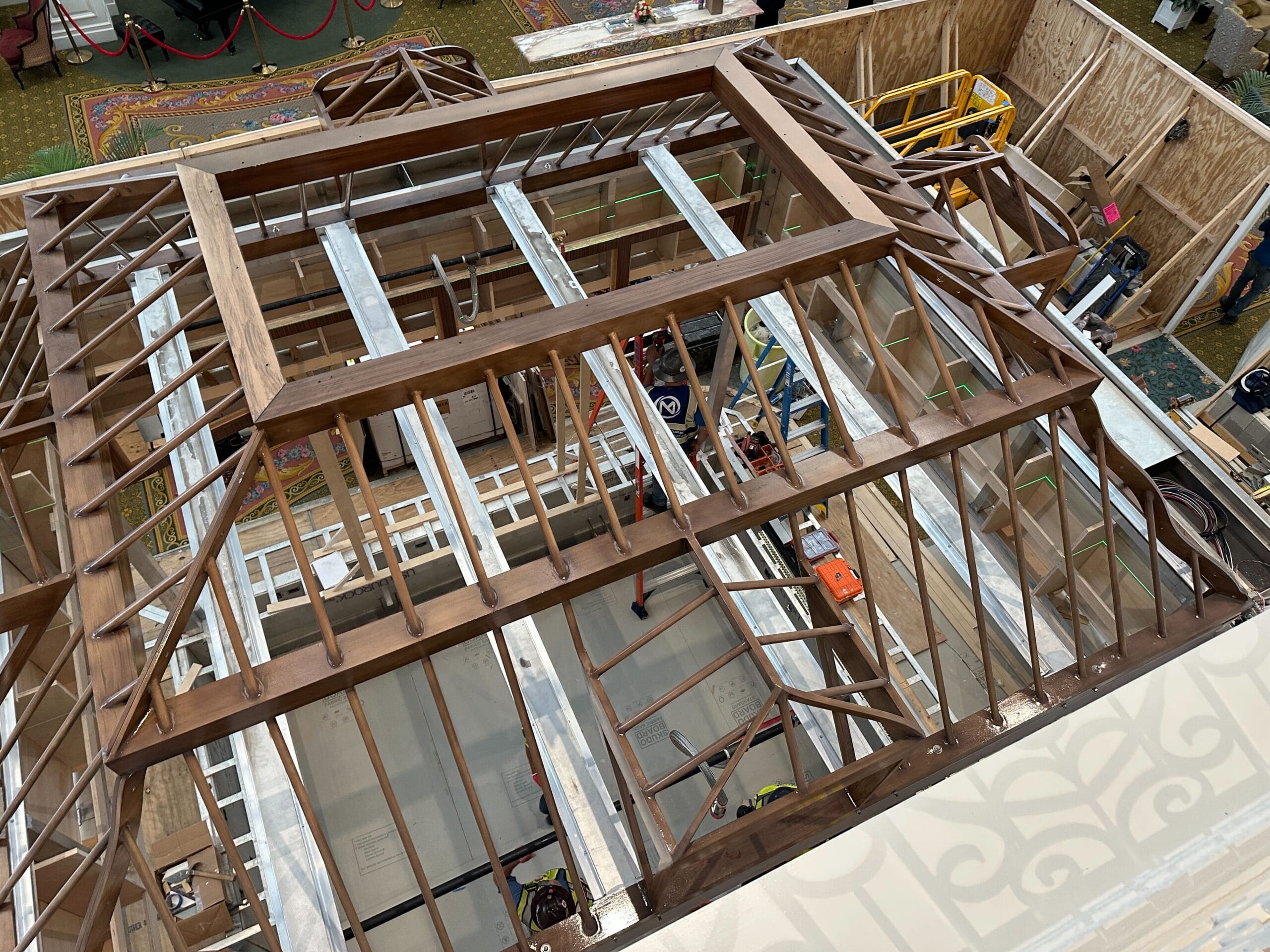 A view from above of a wooden roof frame under construction at the Grand Floridian Resort, with workers and tools visible inside.