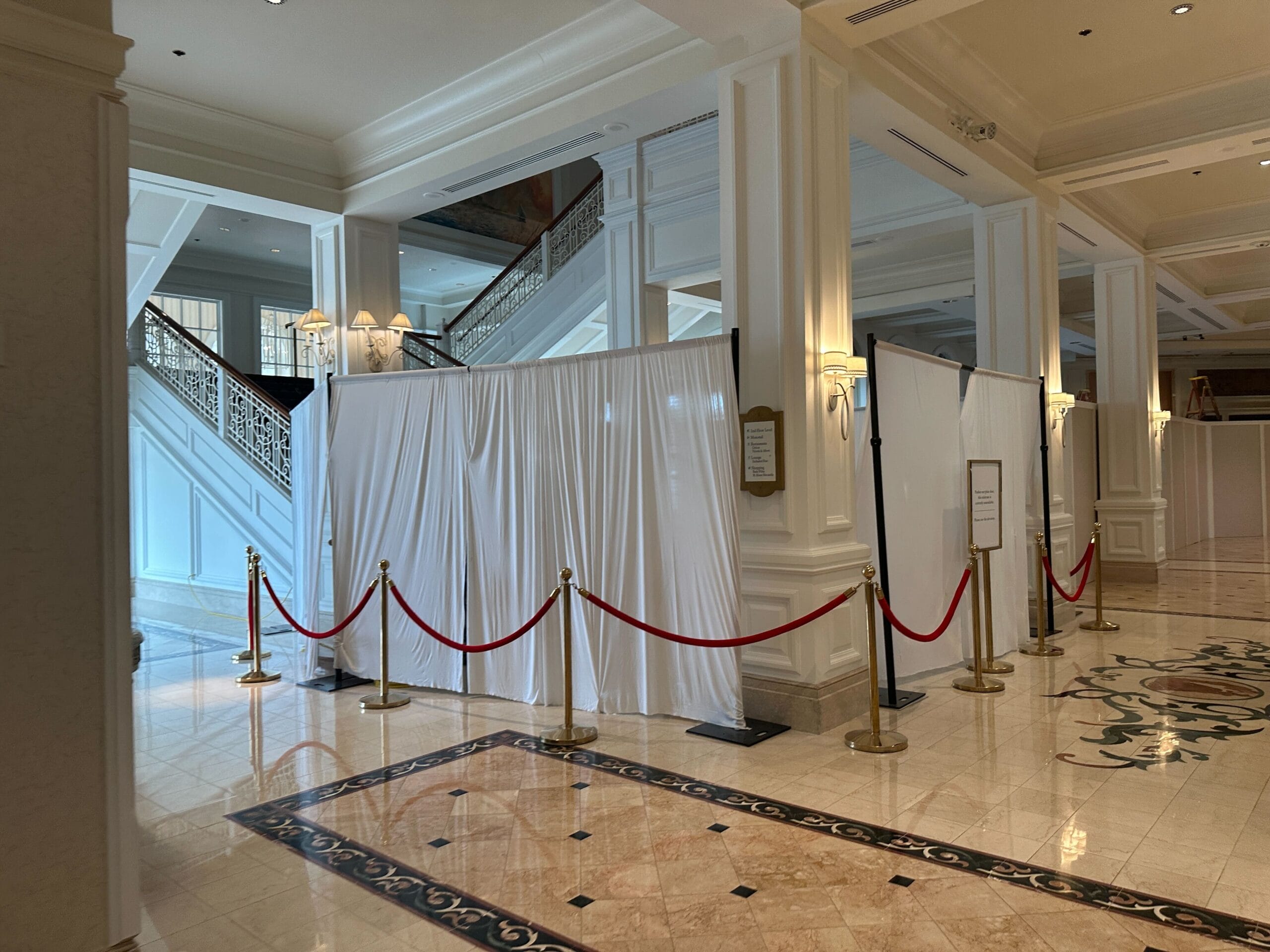 White curtains section off an area in a hotel lobby with marble floors and red rope barriers.