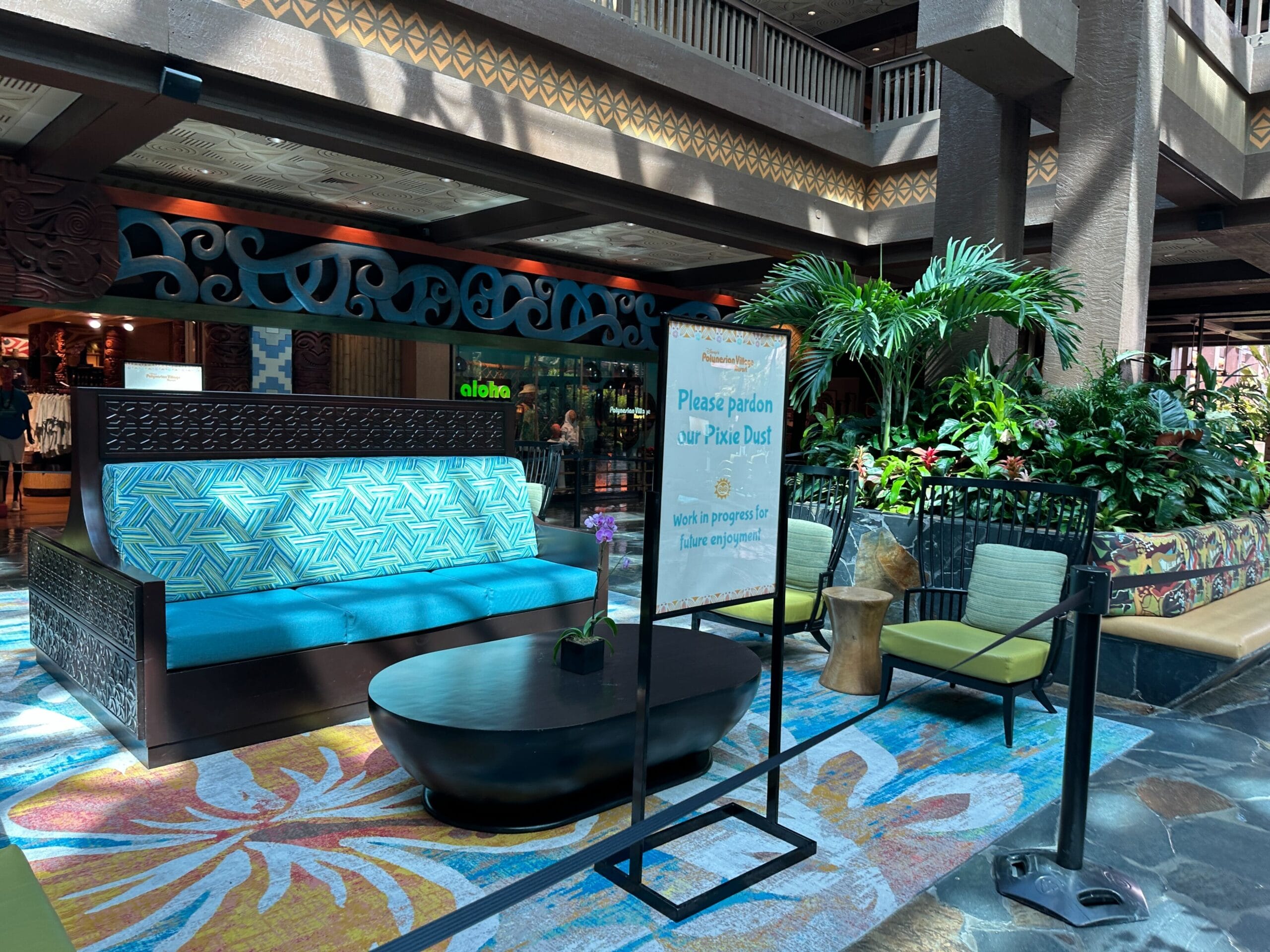 Lobby area with tropical decor, a blue couch, plants, and a sign saying, Please pardon our 'Pixie Dust.'