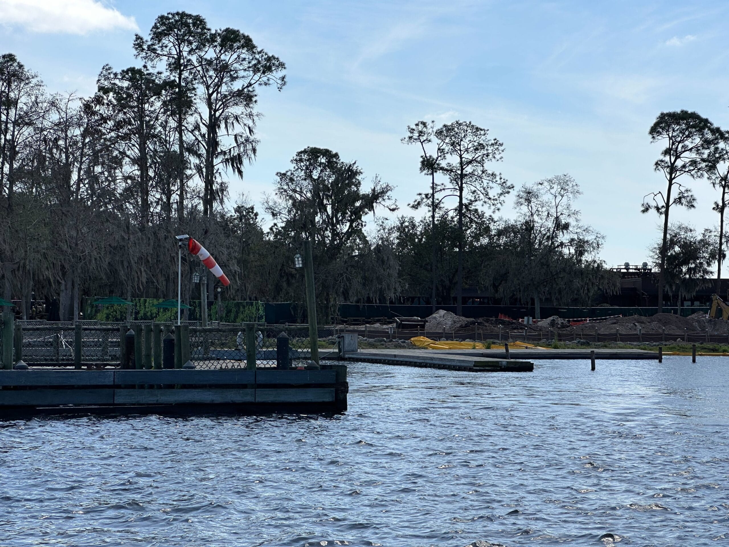 View of a lake with a small dock and a wind sock, while trees and the Lakeshore Lodge construction update unfold in the background.